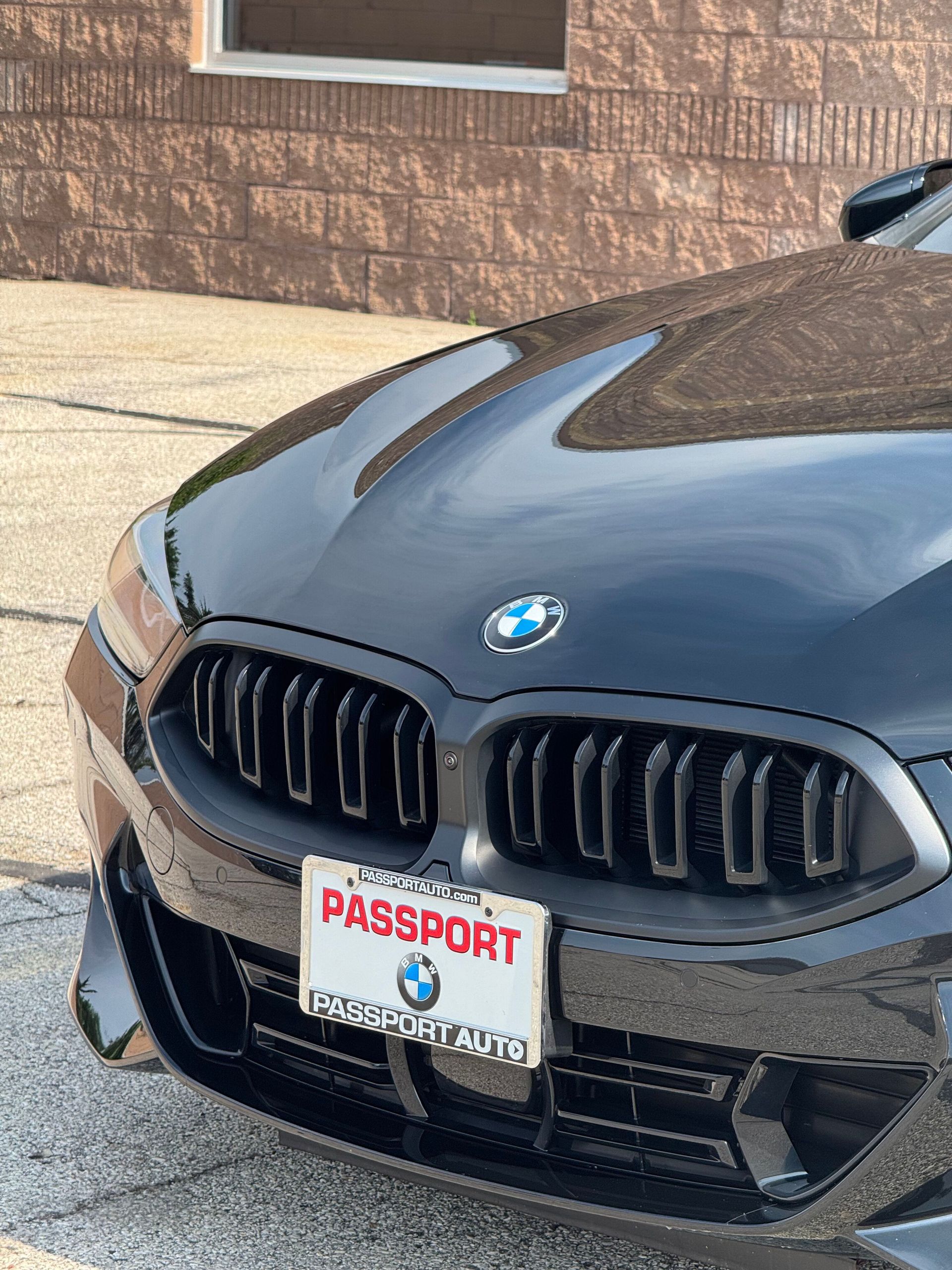 Black BMW car with a Passport dealer license plate in front of a brick building.