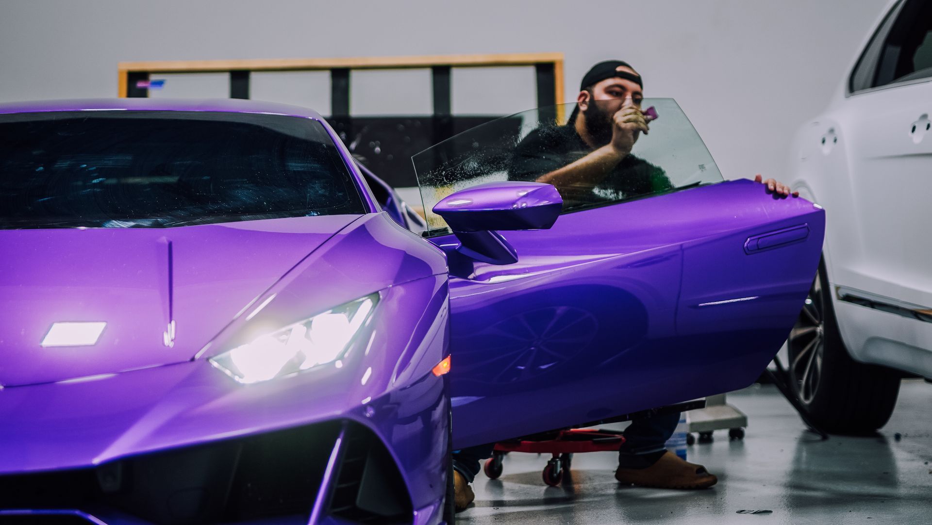 Man installing tint on a purple sports car's window in a garage.