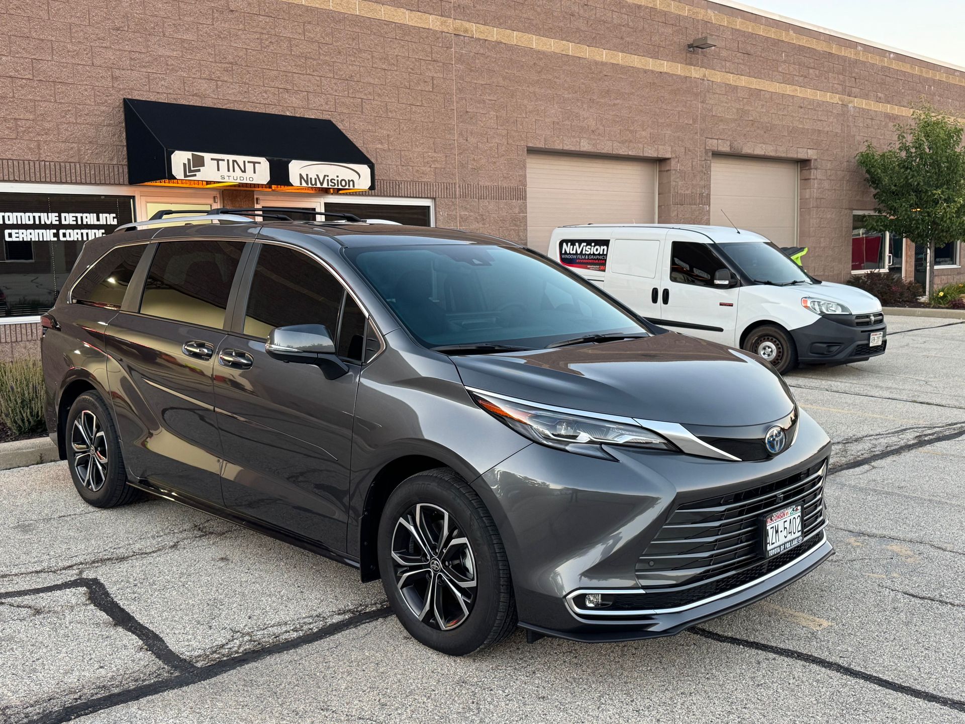 Gray Toyota Sienna minivan parked outside a brick building with a white van.