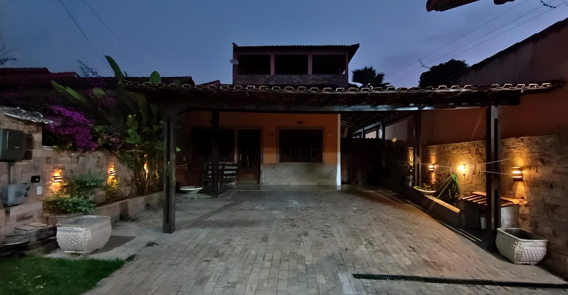 Uma casa com uma entrada de automóveis e uma varanda coberta à noite.