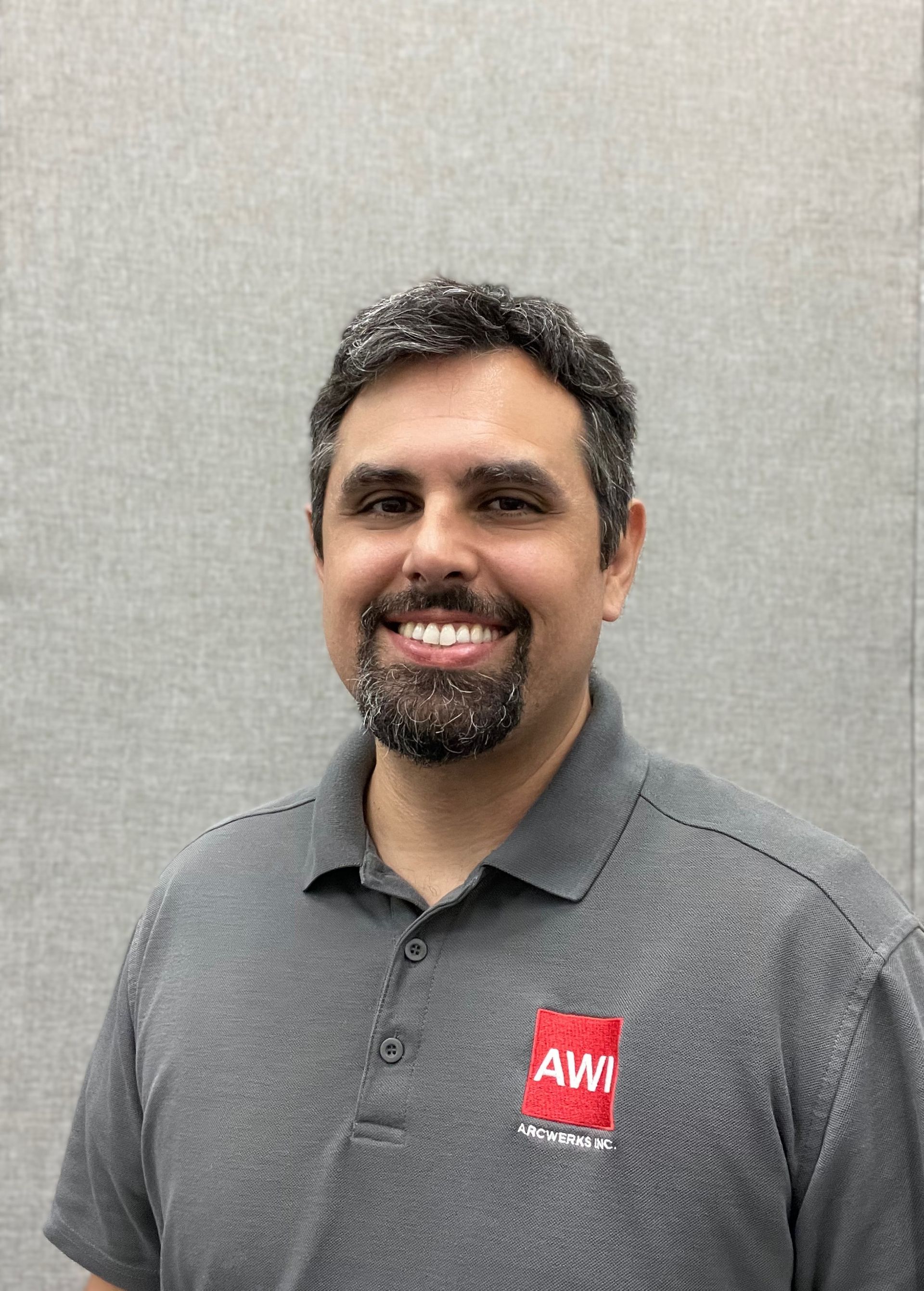 A man with a beard is wearing a gray shirt with a red aw logo on it.