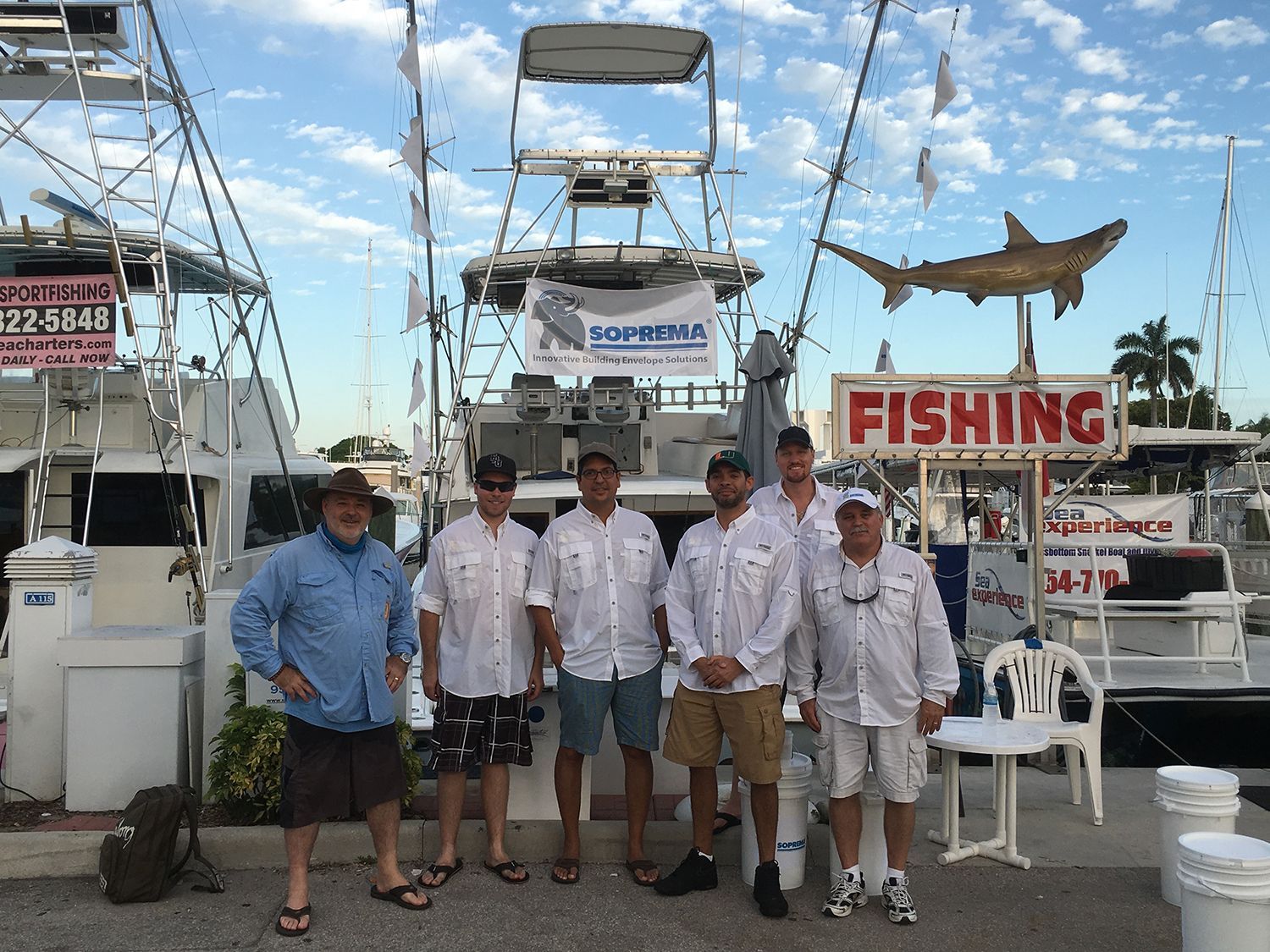 A group of men are posing for a picture in front of a fishing sign.