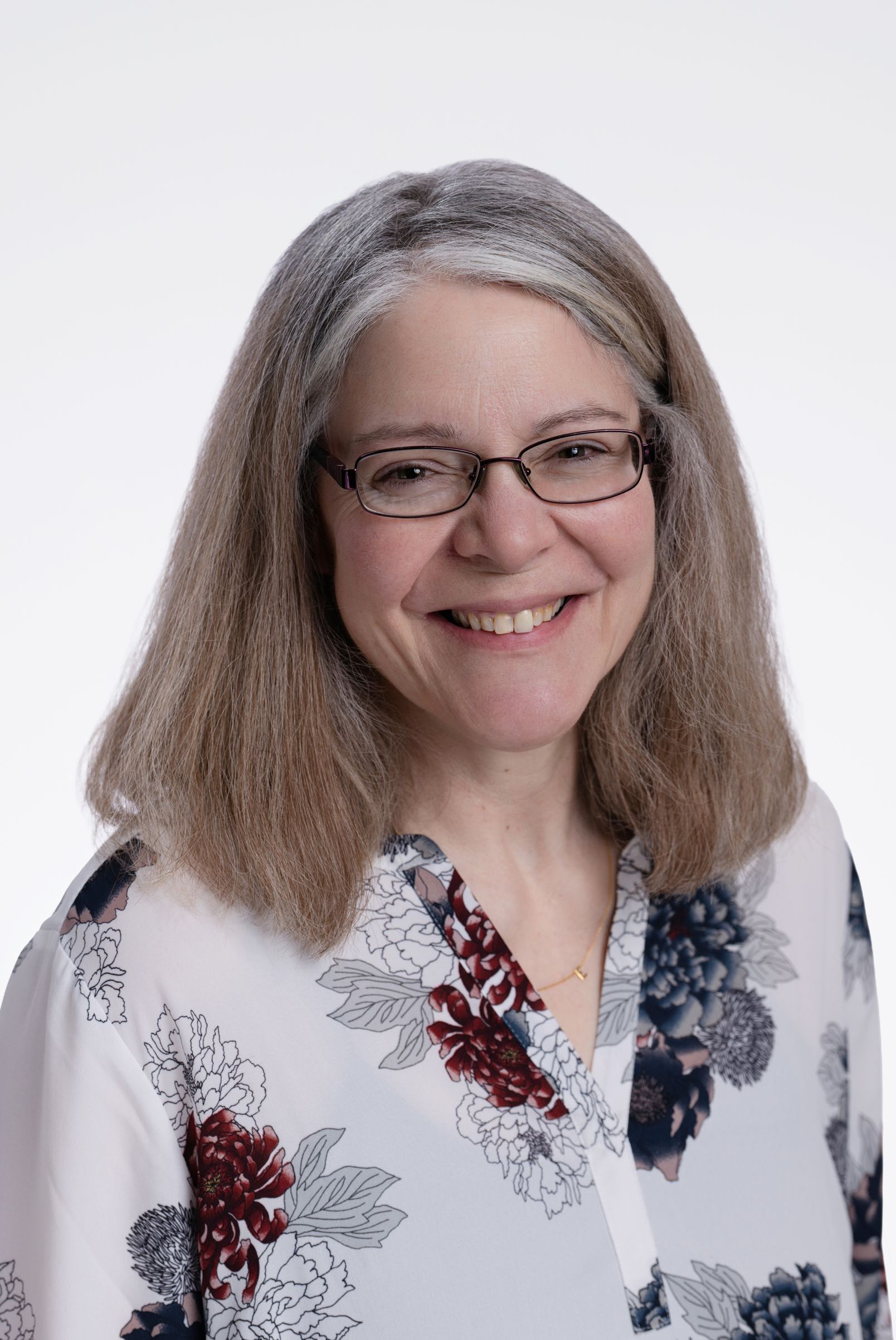 A woman wearing glasses and a floral shirt is smiling for the camera.