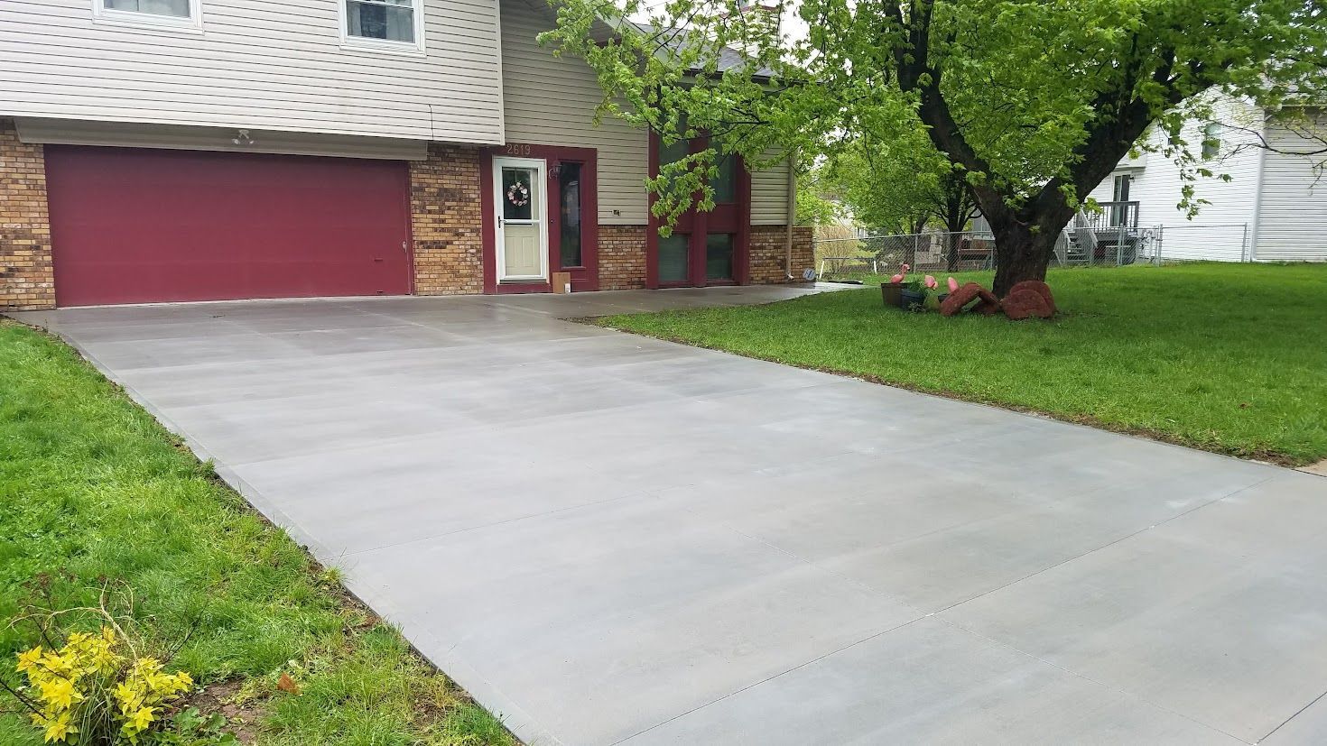 Wet concrete pours from a wooden chute onto a ground surface at a construction site while workers labor in the background.