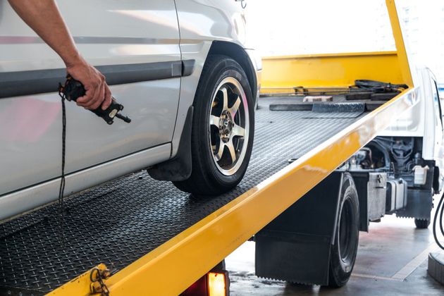 A person uses a handheld remote control to winch a silver car onto a flatbed tow truck.