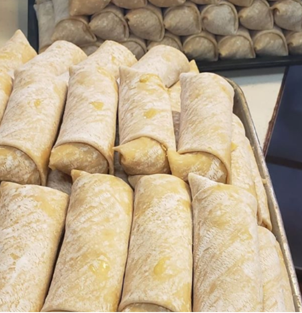 Tray of uncooked spring rolls, close-up view. Background has a row of dumplings.