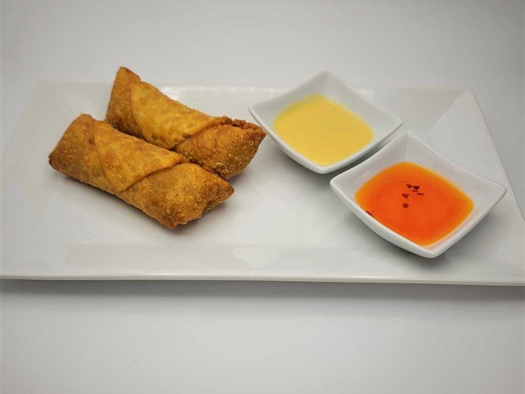 Two egg rolls with two dipping sauces on a white rectangular plate.