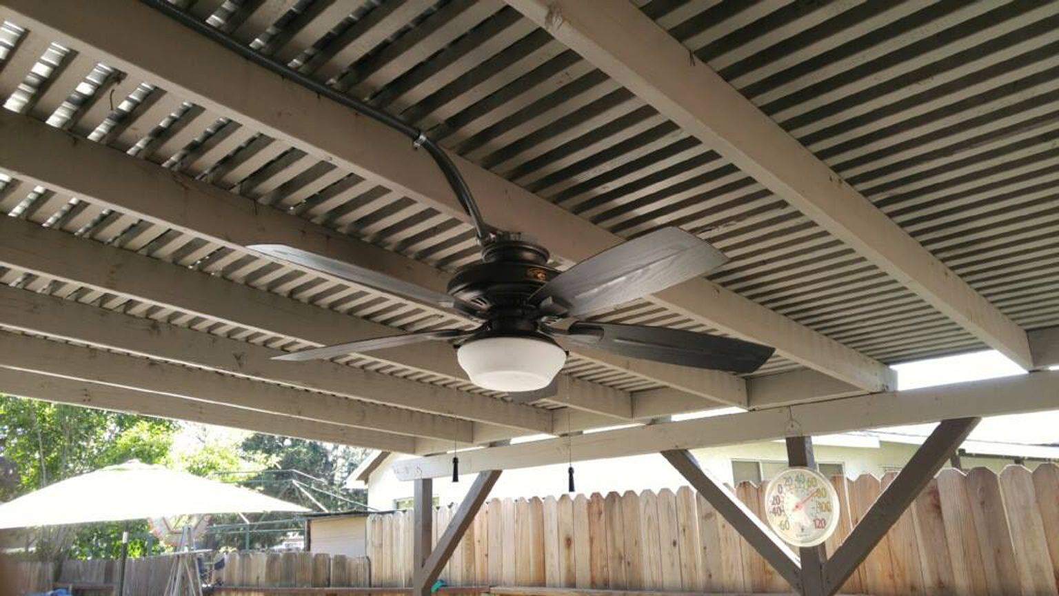A ceiling fan is hanging from the ceiling of a pergola.