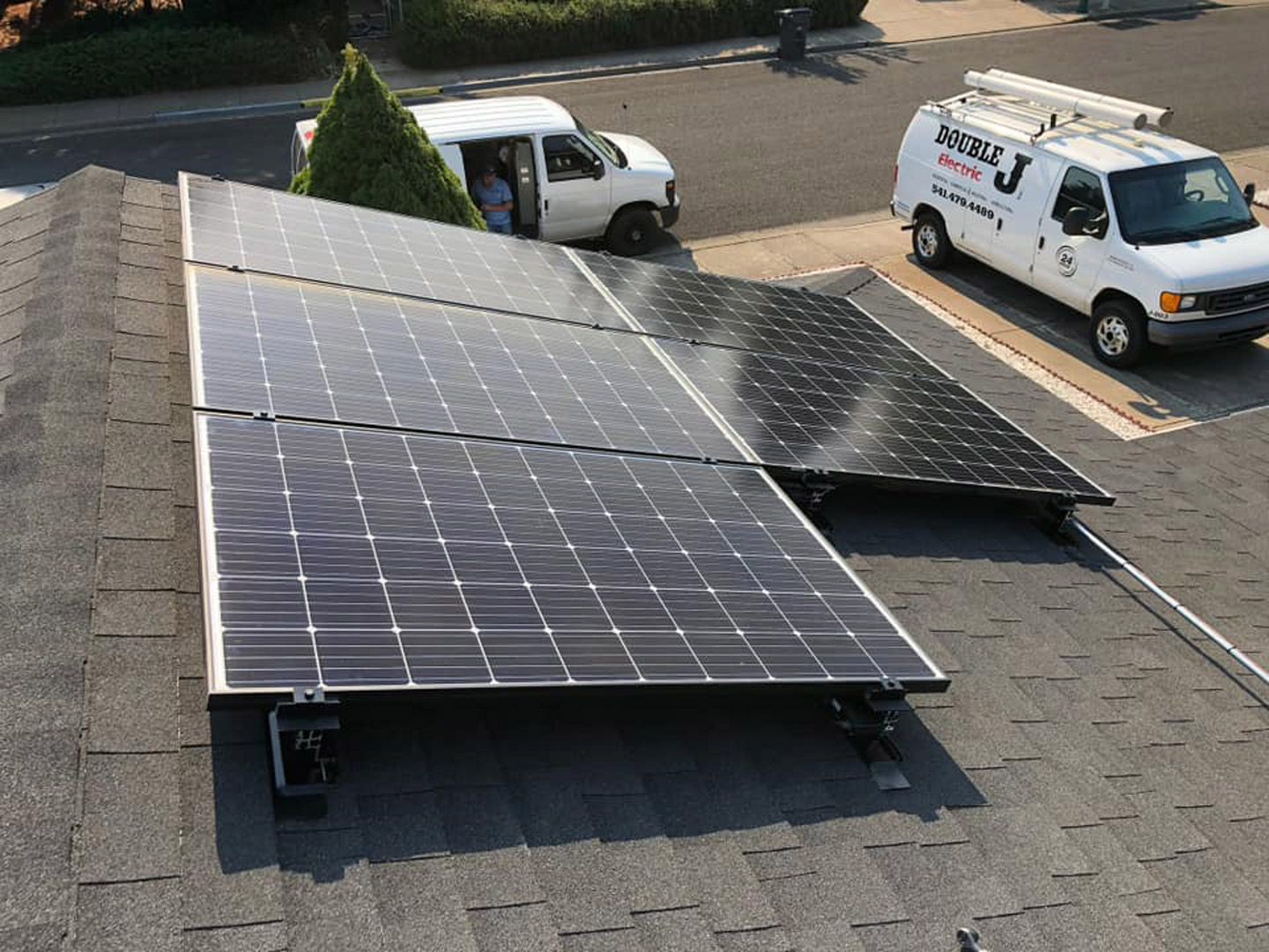 A white van with the letter j on the side is parked next to a row of solar panels on a roof