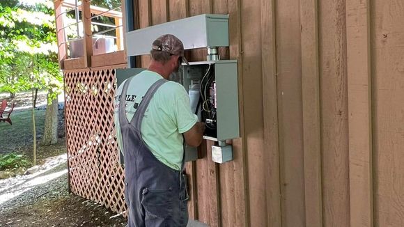 A man is working on an electrical box on the side of a house.