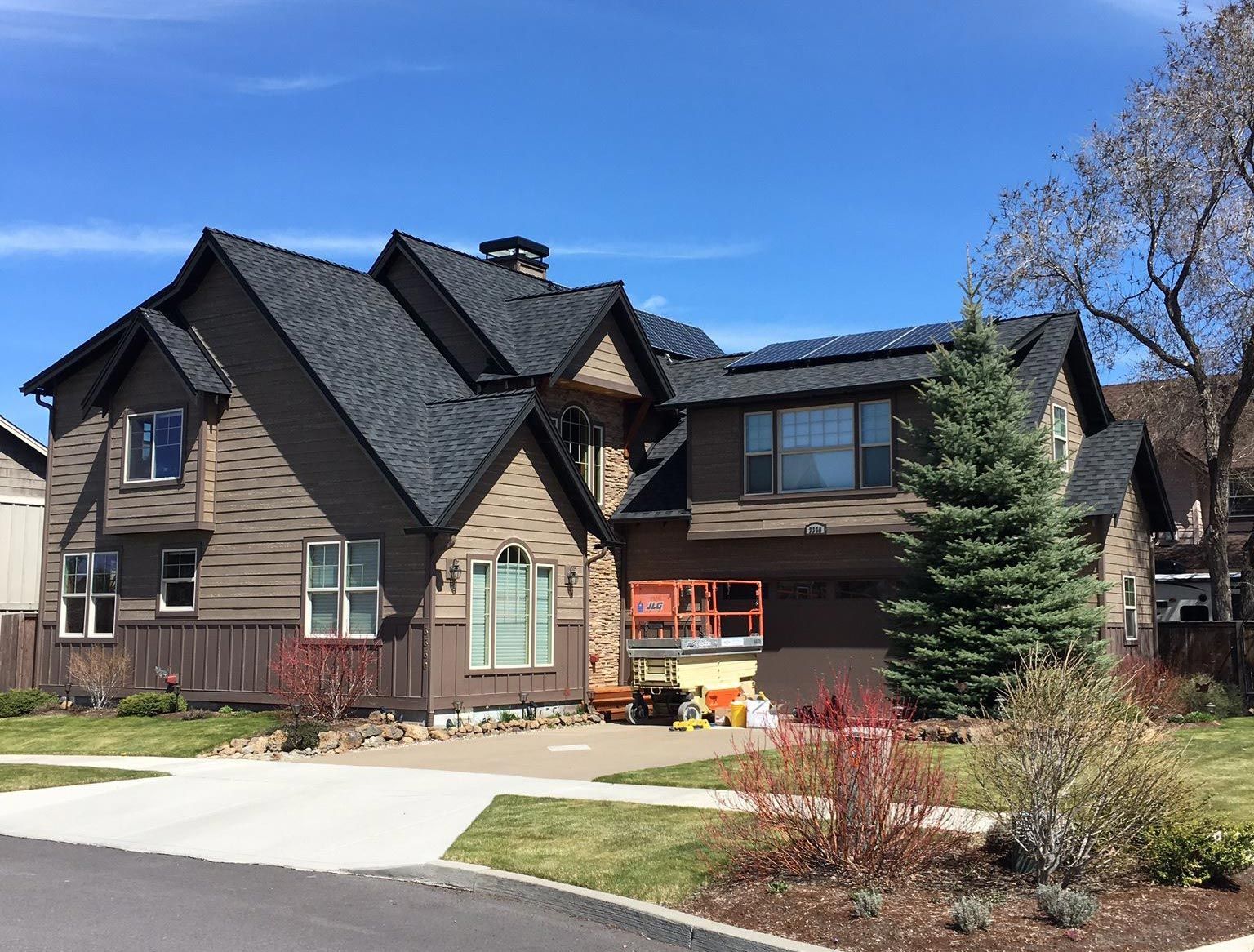 A large house with a black roof is sitting on top of a lush green hillside.
