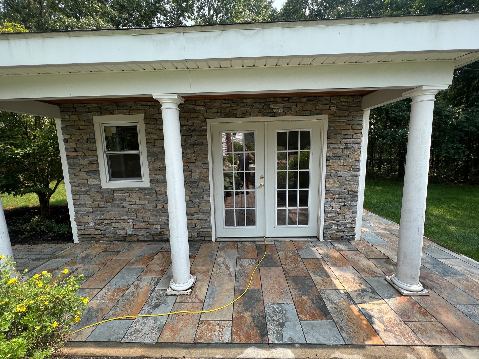 Stone porch with white columns, French doors, and a patterned patio floor in front of a small building