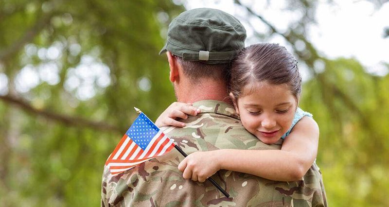a little girl hugging a soldier with an american flag on his back