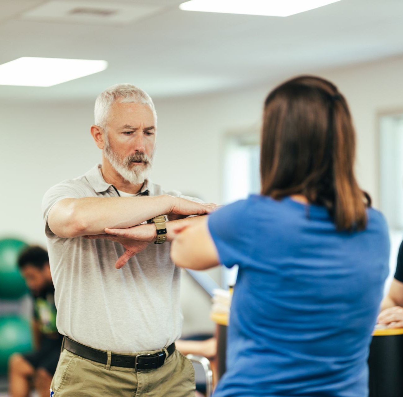 Woman with long dark hair using laptop at a table, books in front of her. Bright room, focus on the screen.