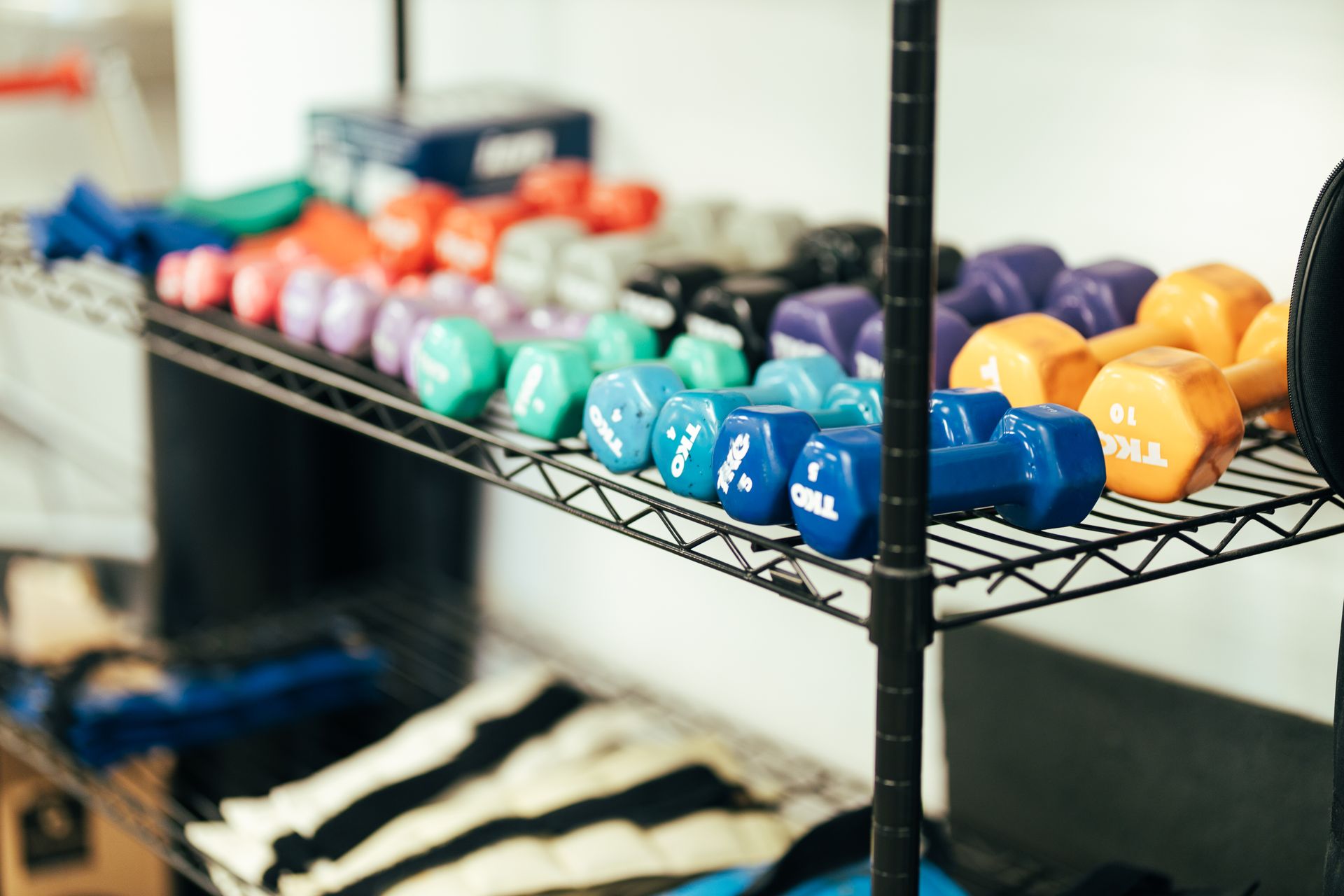 Rows of colorful dumbbells on a black wire shelf in a gym.