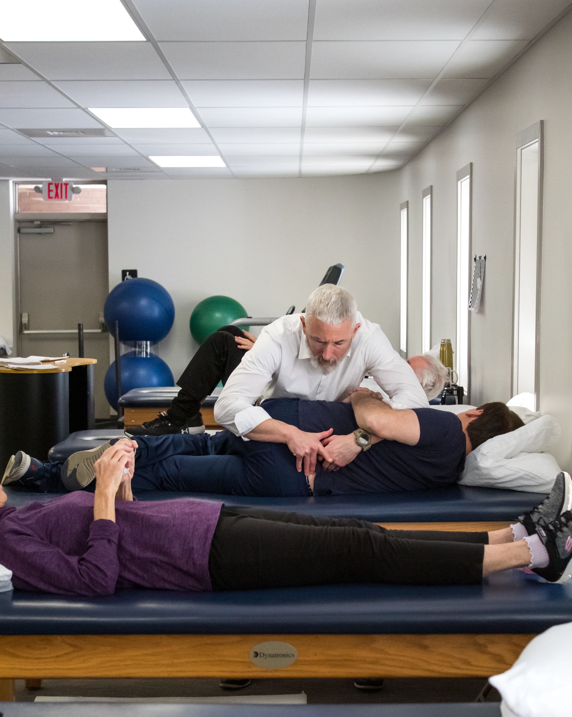 Physical therapist working with a patient on a treatment table. Another patient is in the foreground. Clinic setting.