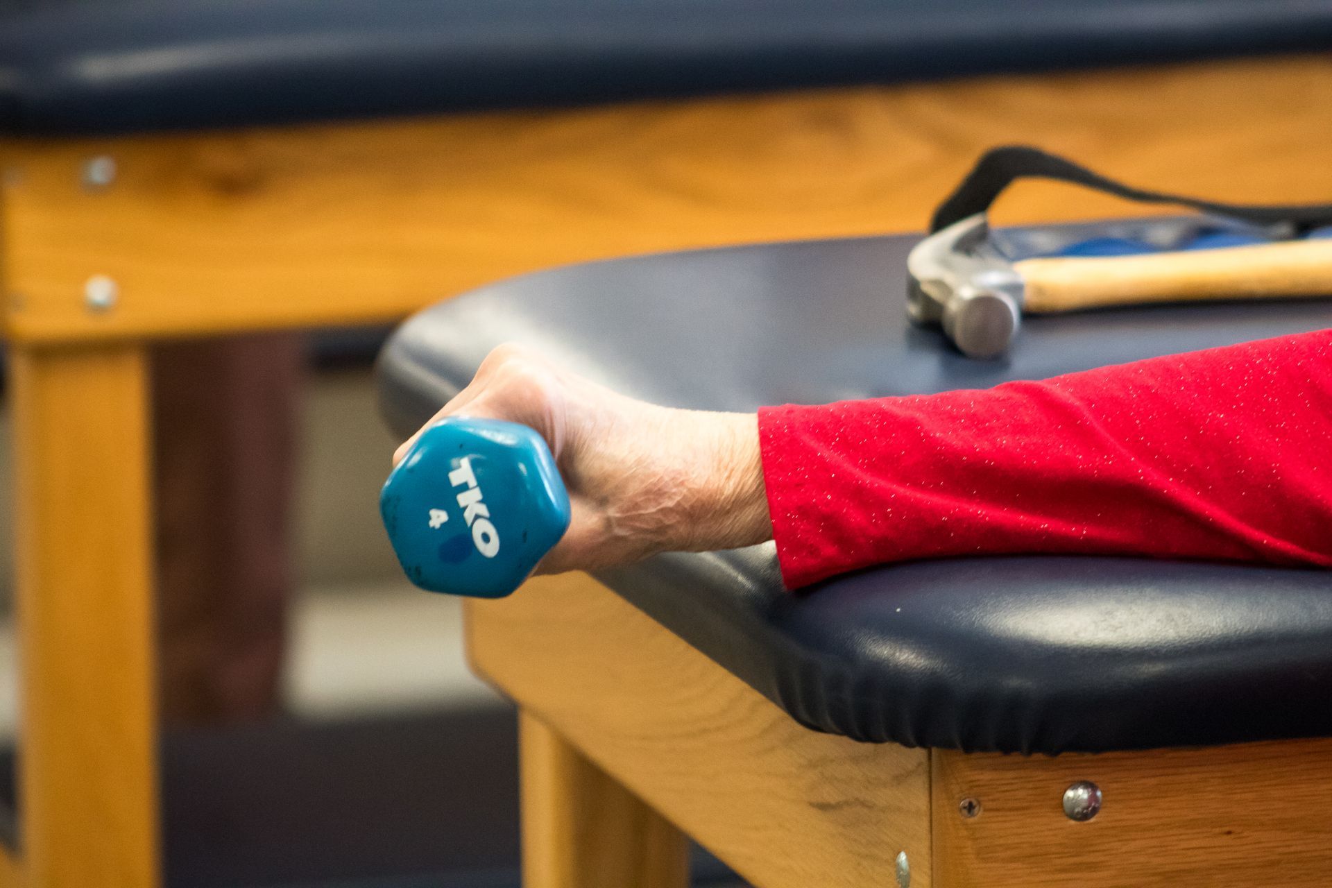 Person holding a blue 4-lb dumbbell, resting arm on a blue padded table. A hammer is in the background.