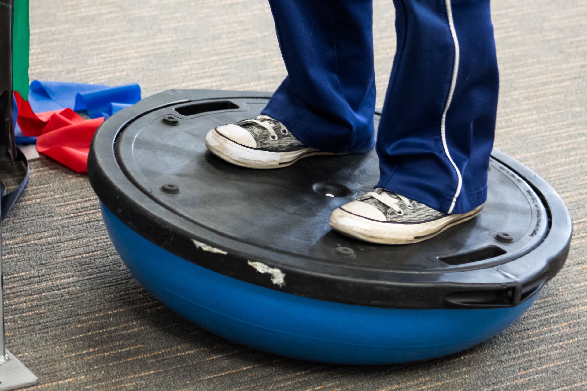 Person standing on a blue and black balance trainer, wearing blue pants and sneakers.