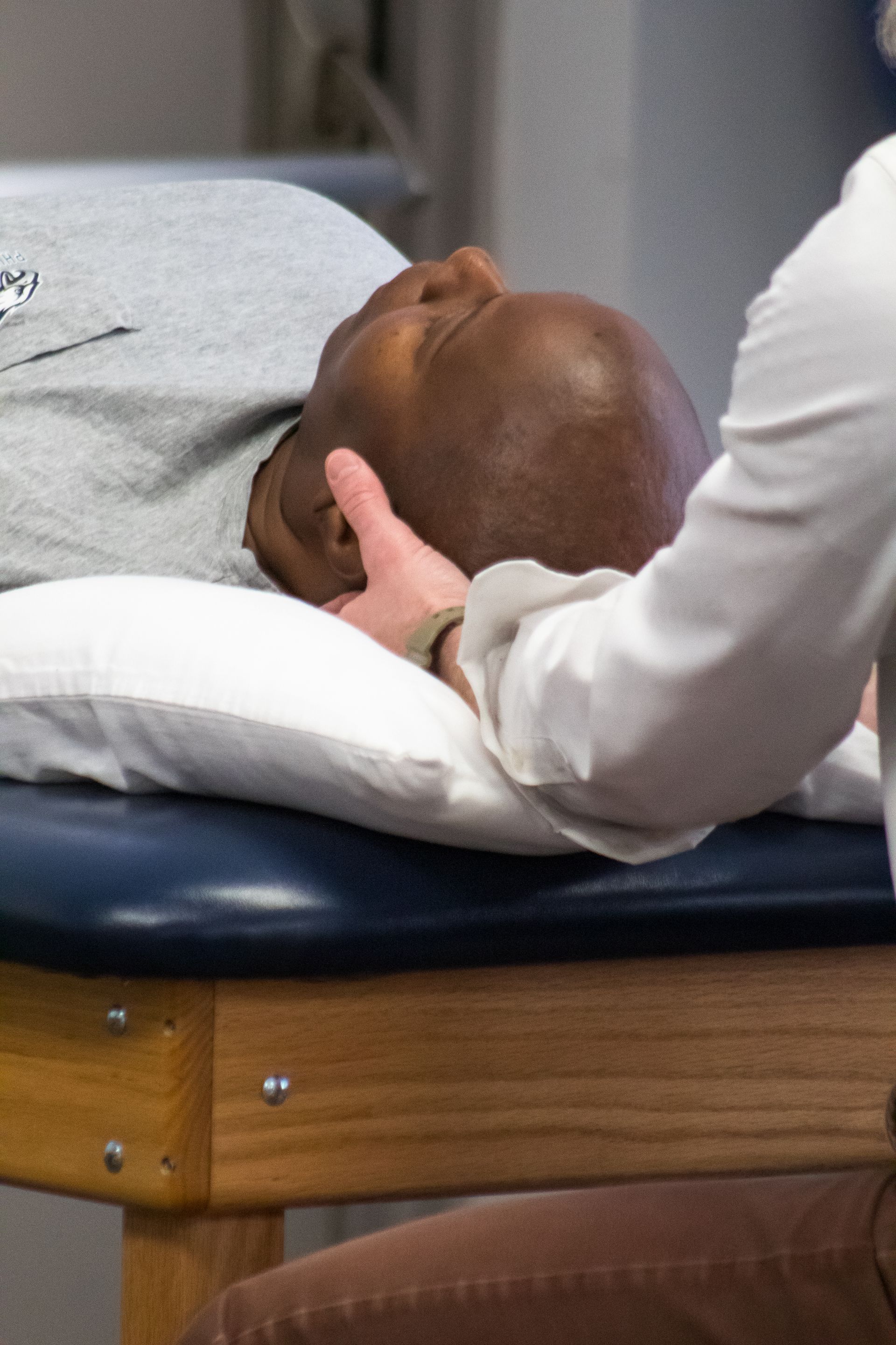 A person's head being examined by a professional. The person lies on a pillow, receiving a head adjustment.