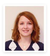 Woman with auburn hair smiles, wearing a navy sweater with white accents.