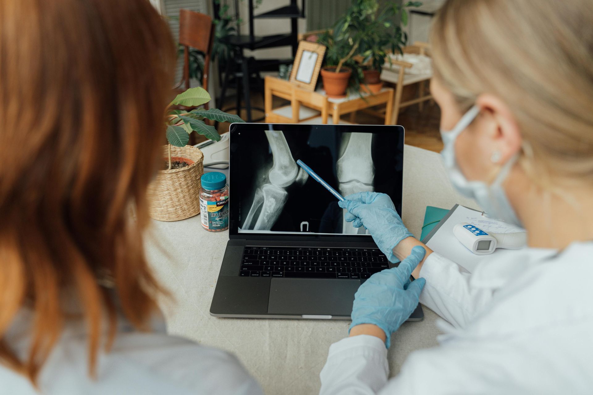 Doctor in blue gloves pointing at knee X-ray on laptop, explaining to a patient.