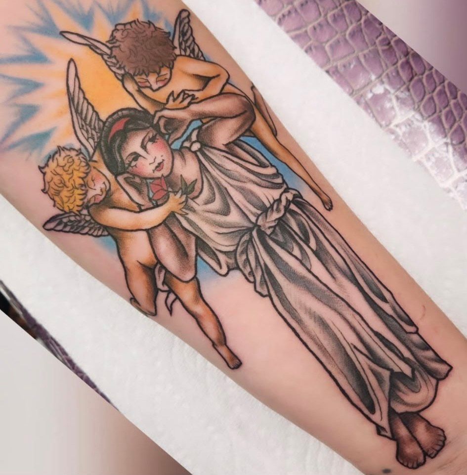 Tattoo of a woman in flowing white dress, held by two cherubs, with a yellow sunburst background.