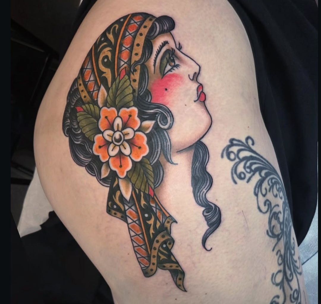 Tattoo of a woman with a headscarf and flower in her hair, looking up with rosy cheeks.