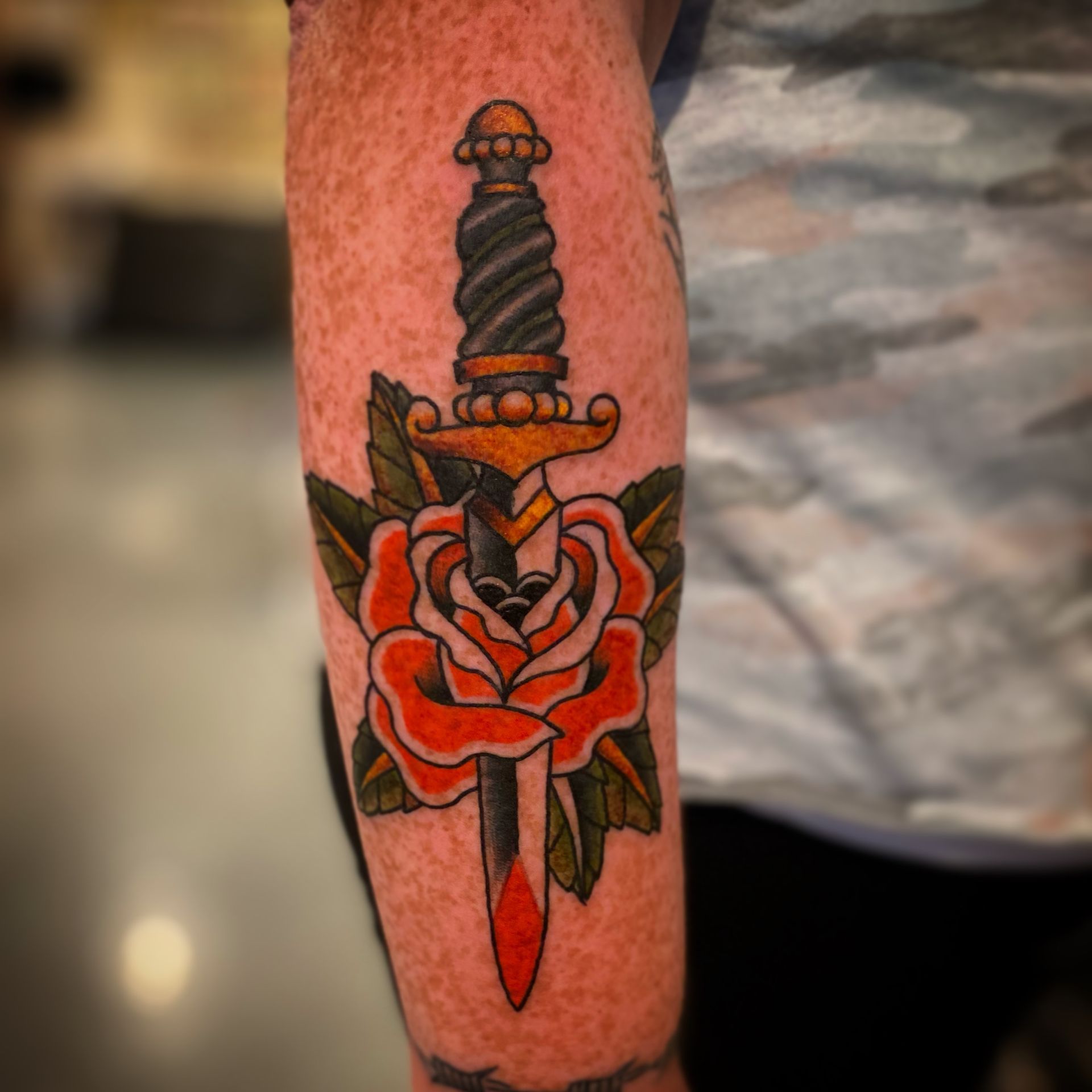 Traditional American dagger with a rose tattoo, done by one of the best tattoo artists in Raleigh NC at a local tattoo parlor