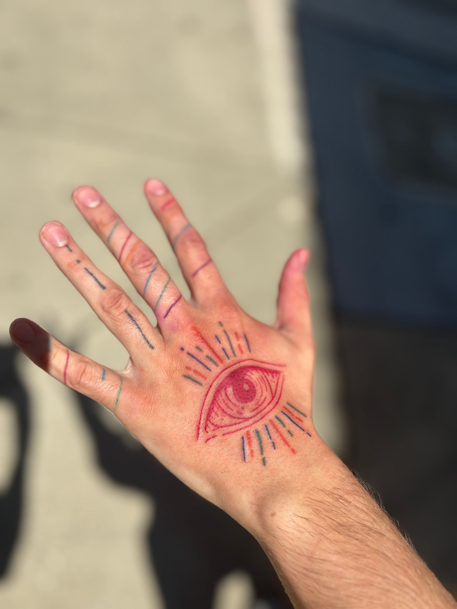 Hand with red all-seeing eye design. Other lines on fingers. Sunny outdoor setting.