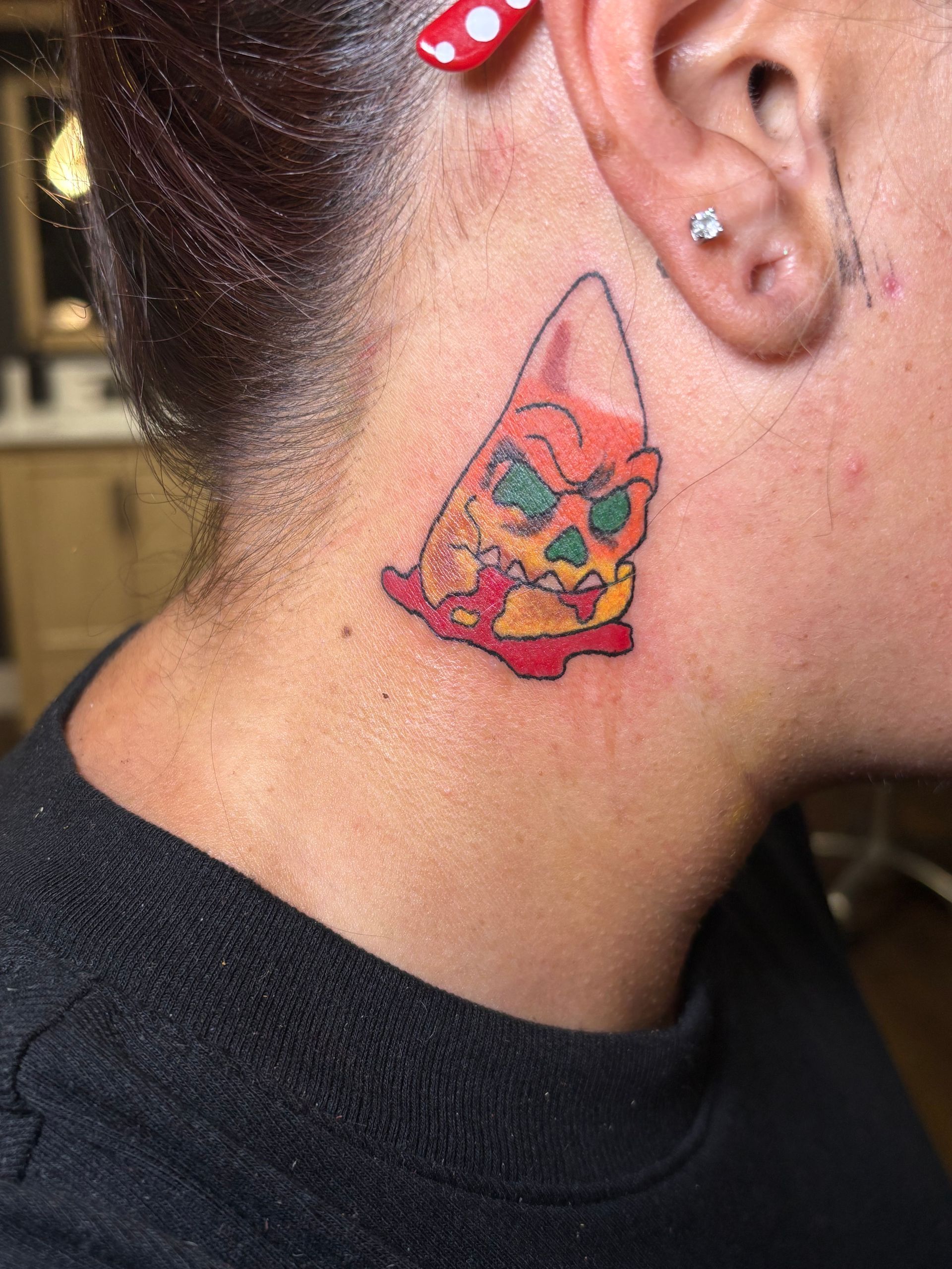 Tattoo of a cartoon skull on the back of a neck, with red, orange, and green coloring.