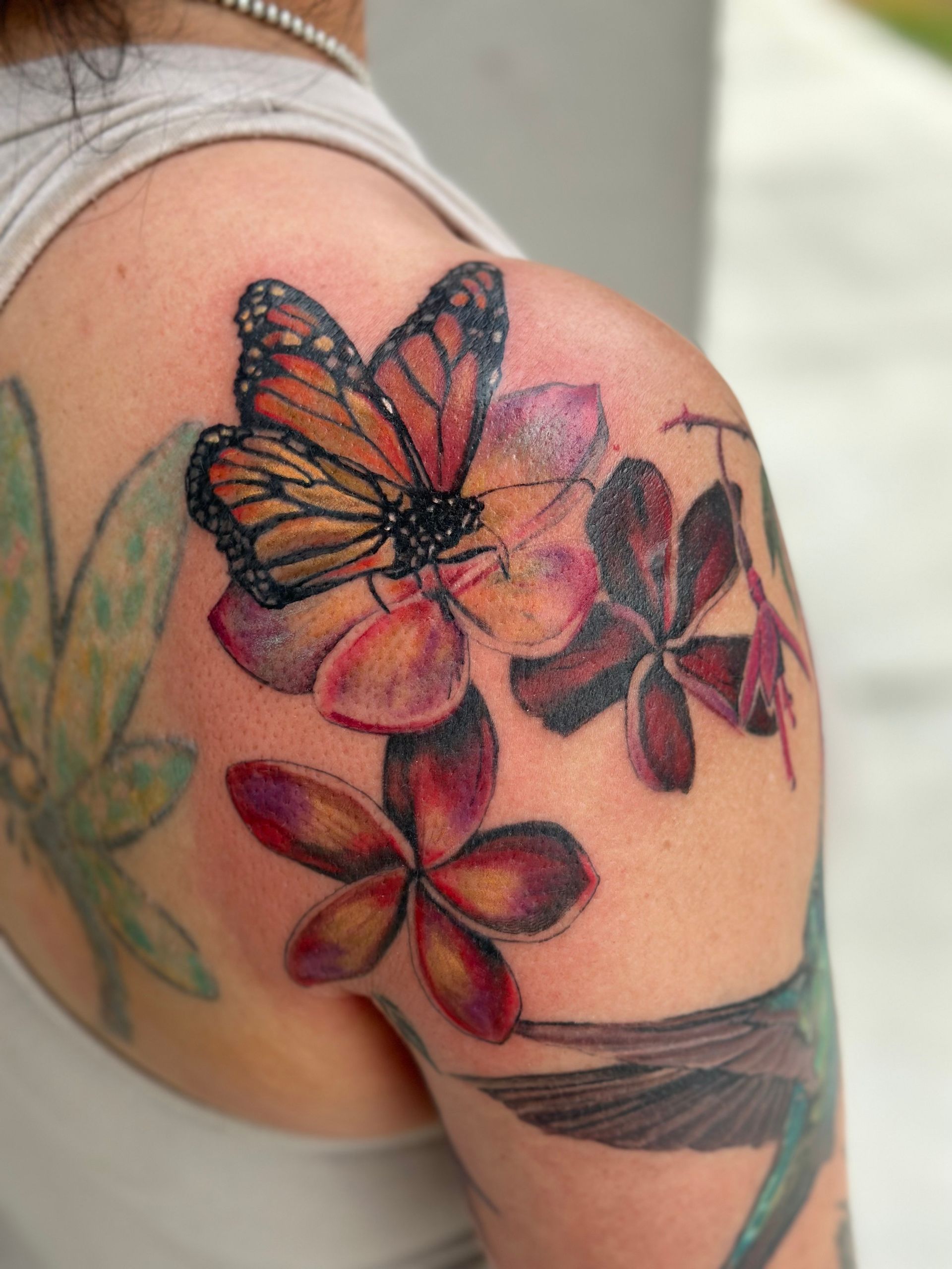 A woman has a tattoo of a butterfly and flowers on her shoulder.