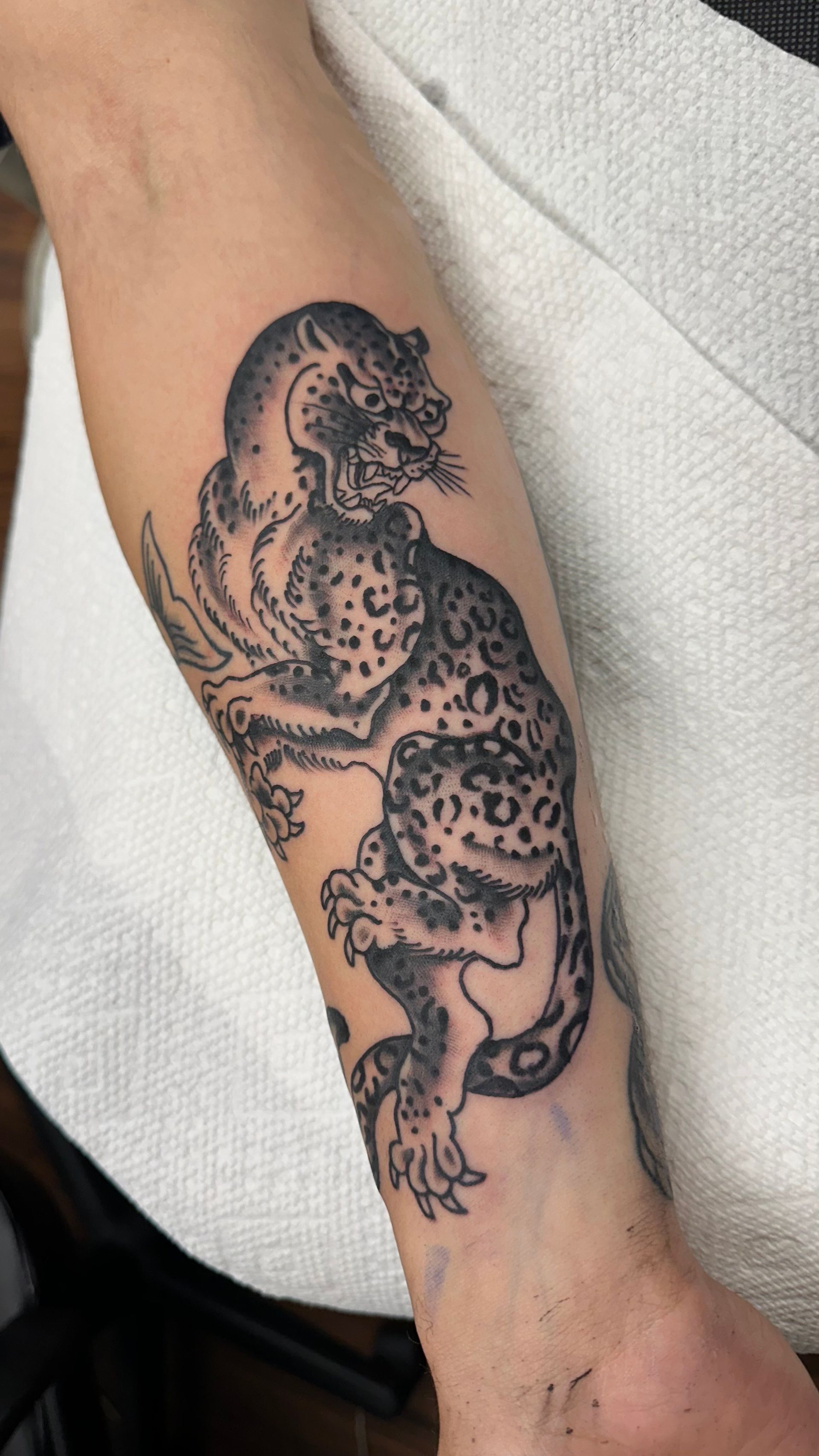 Tattoo of a black leopard on a forearm; it's crouched and has spots with a detailed design.