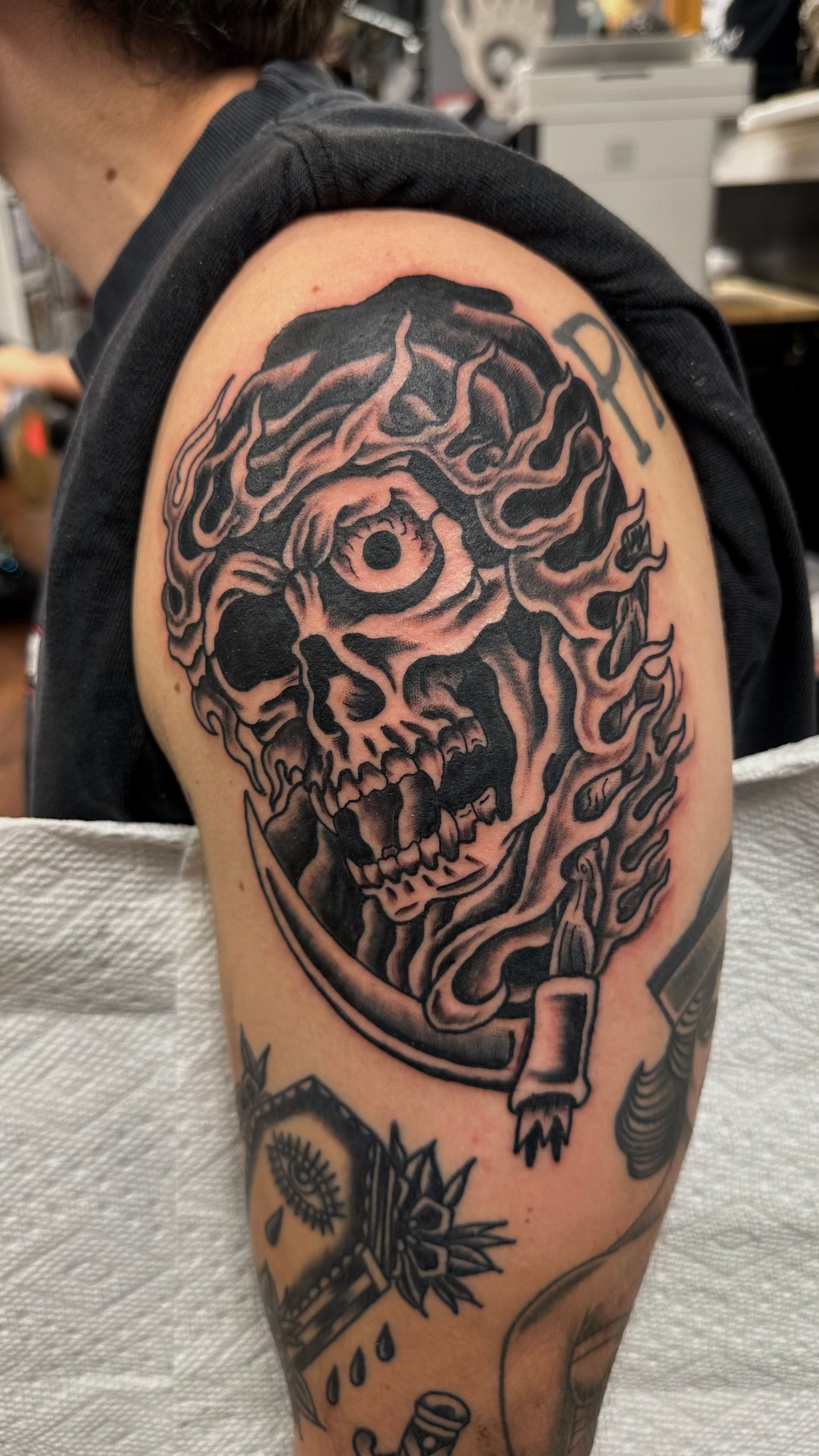 Skull tattoo with flaming hair on upper arm, shaded in black and grey.