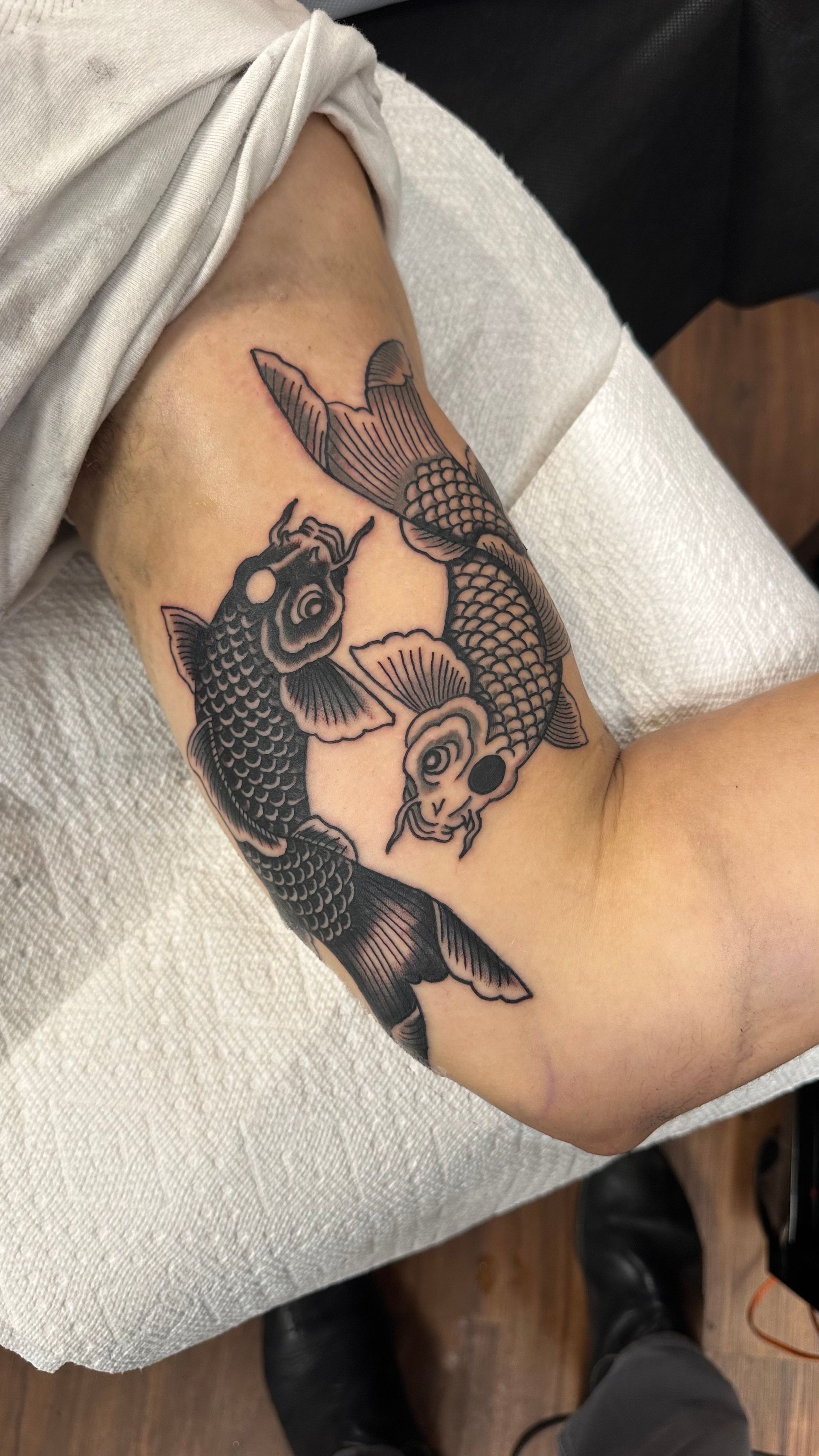 Tattoo of two koi fish in black ink on a person's upper arm.