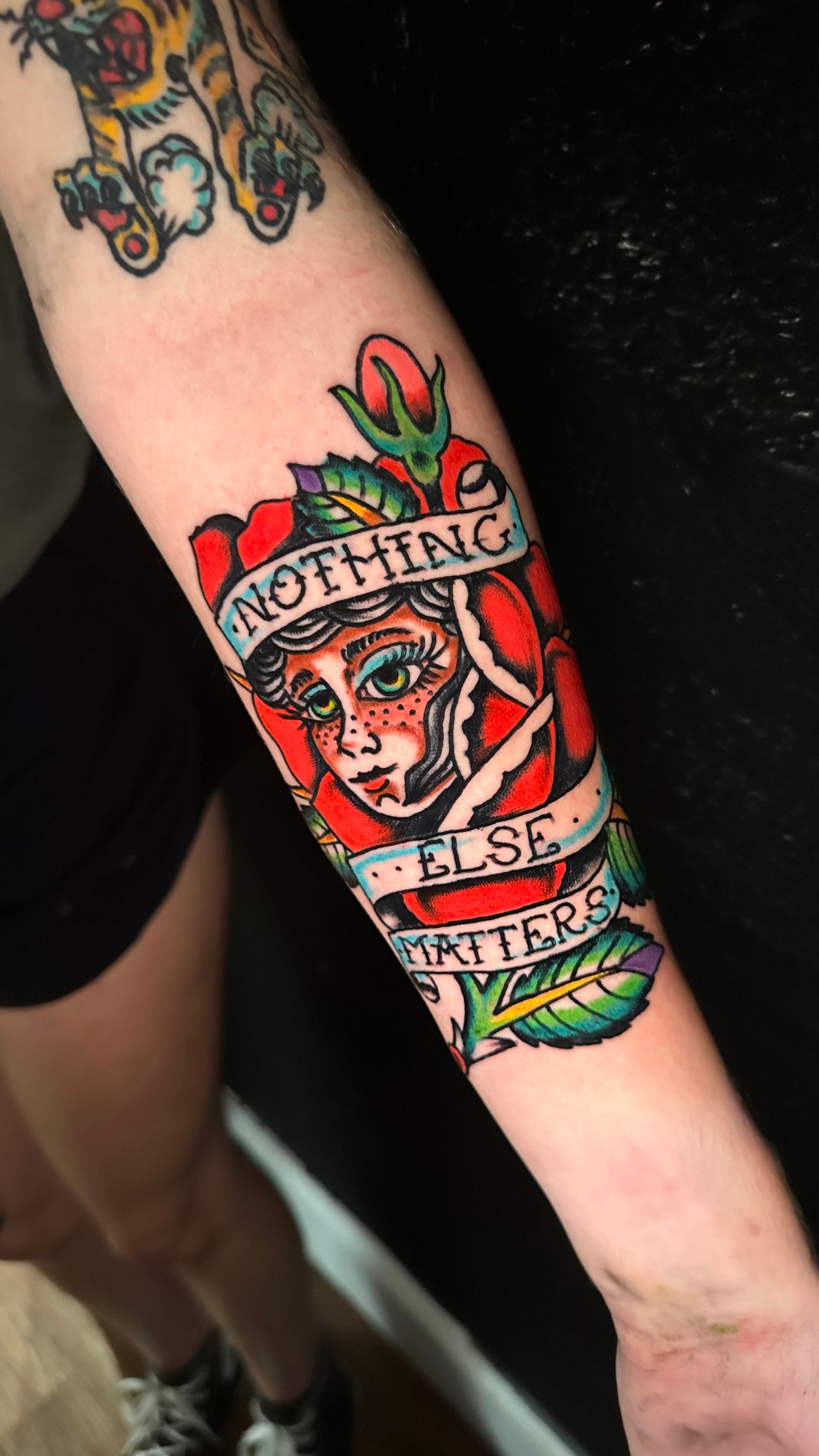Tattoo on forearm: woman's face within a rose, with banner reading