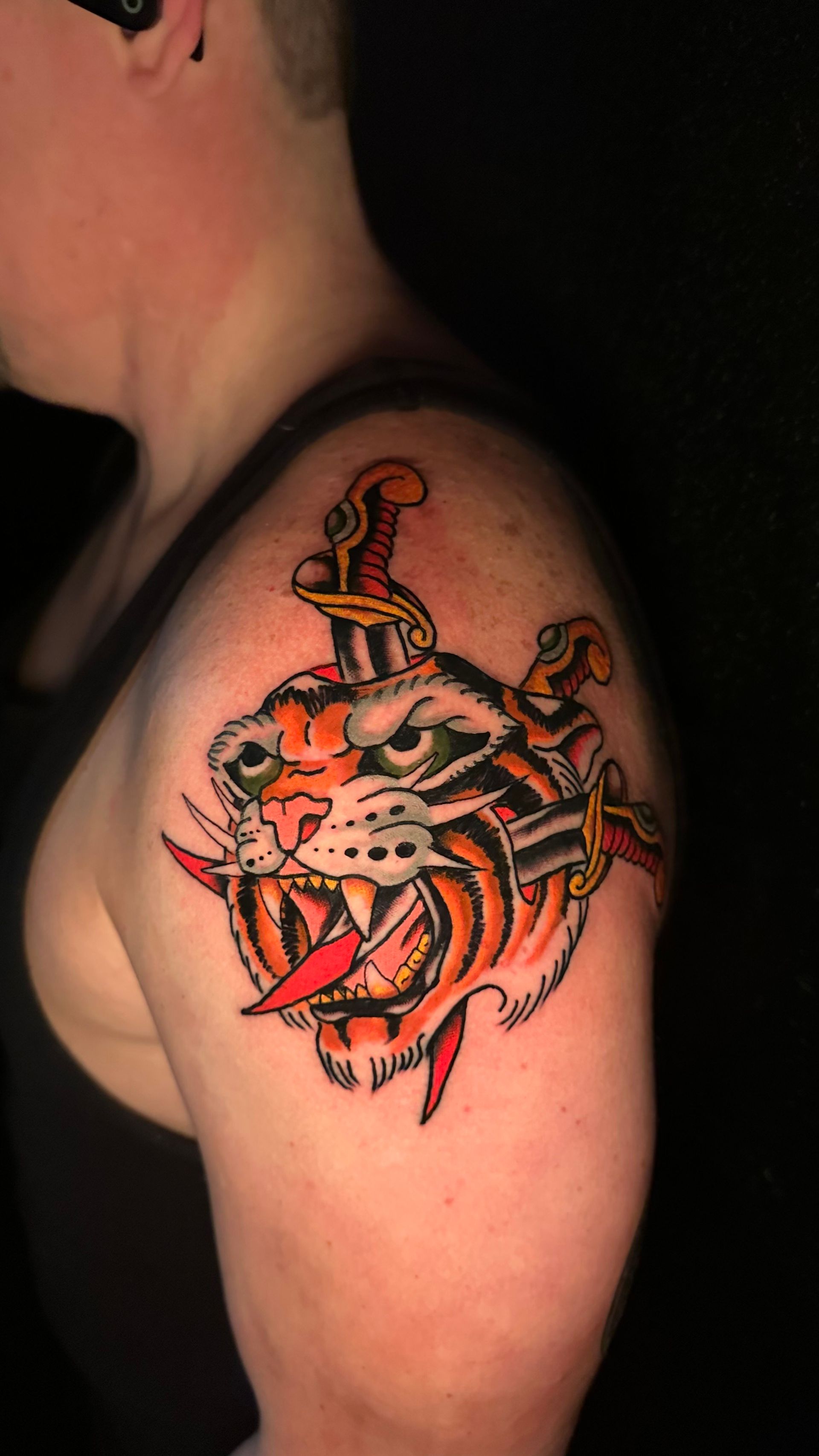 Tiger head tattoo with daggers on a person's shoulder, orange, red, black and green colors.