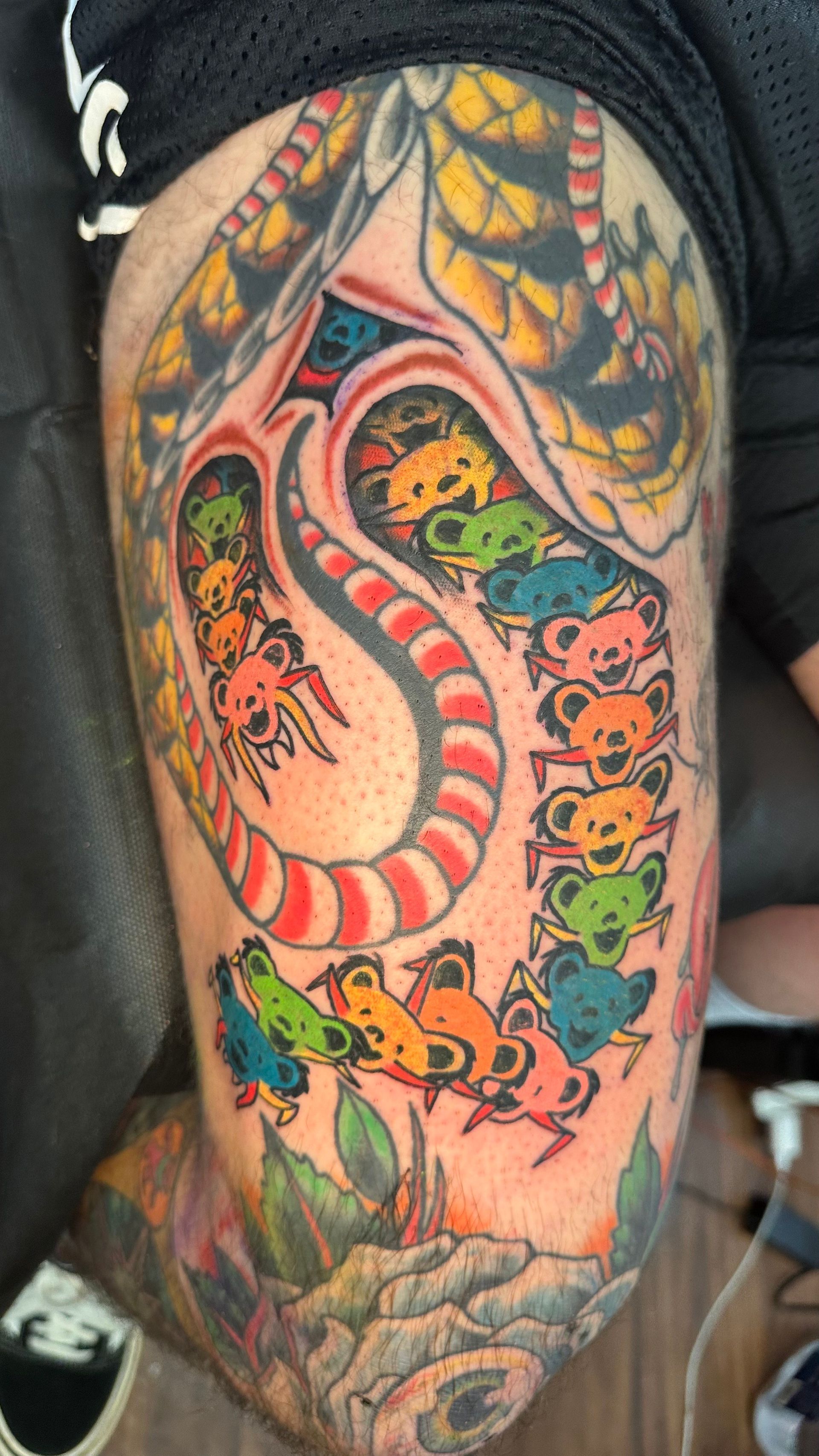 Tattoo of a spine with colorful dancing bears, framed by a snake and body cavity on a person's leg.