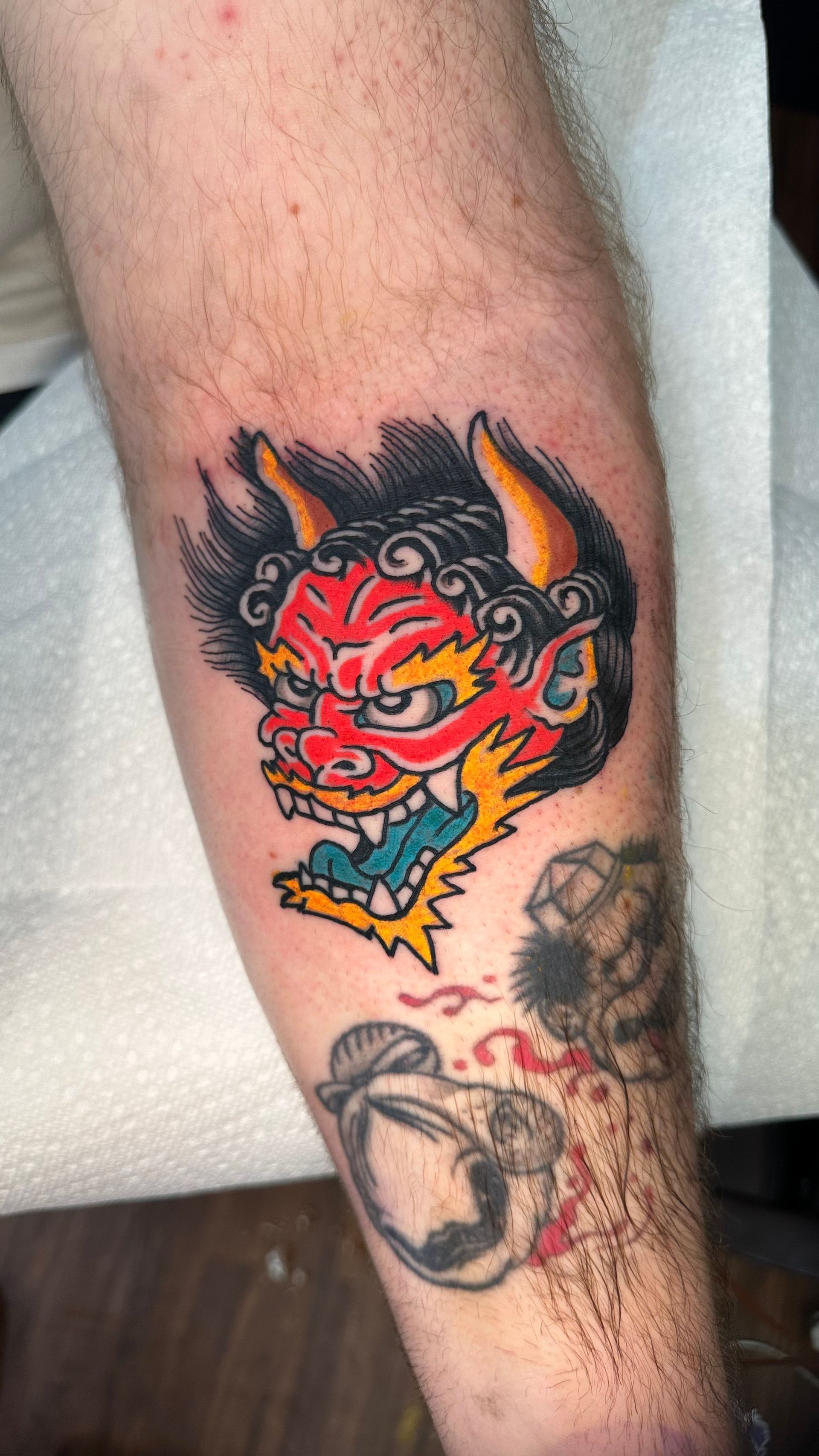 Tattoo of a red, horned demon with sharp teeth and yellow accents on forearm.