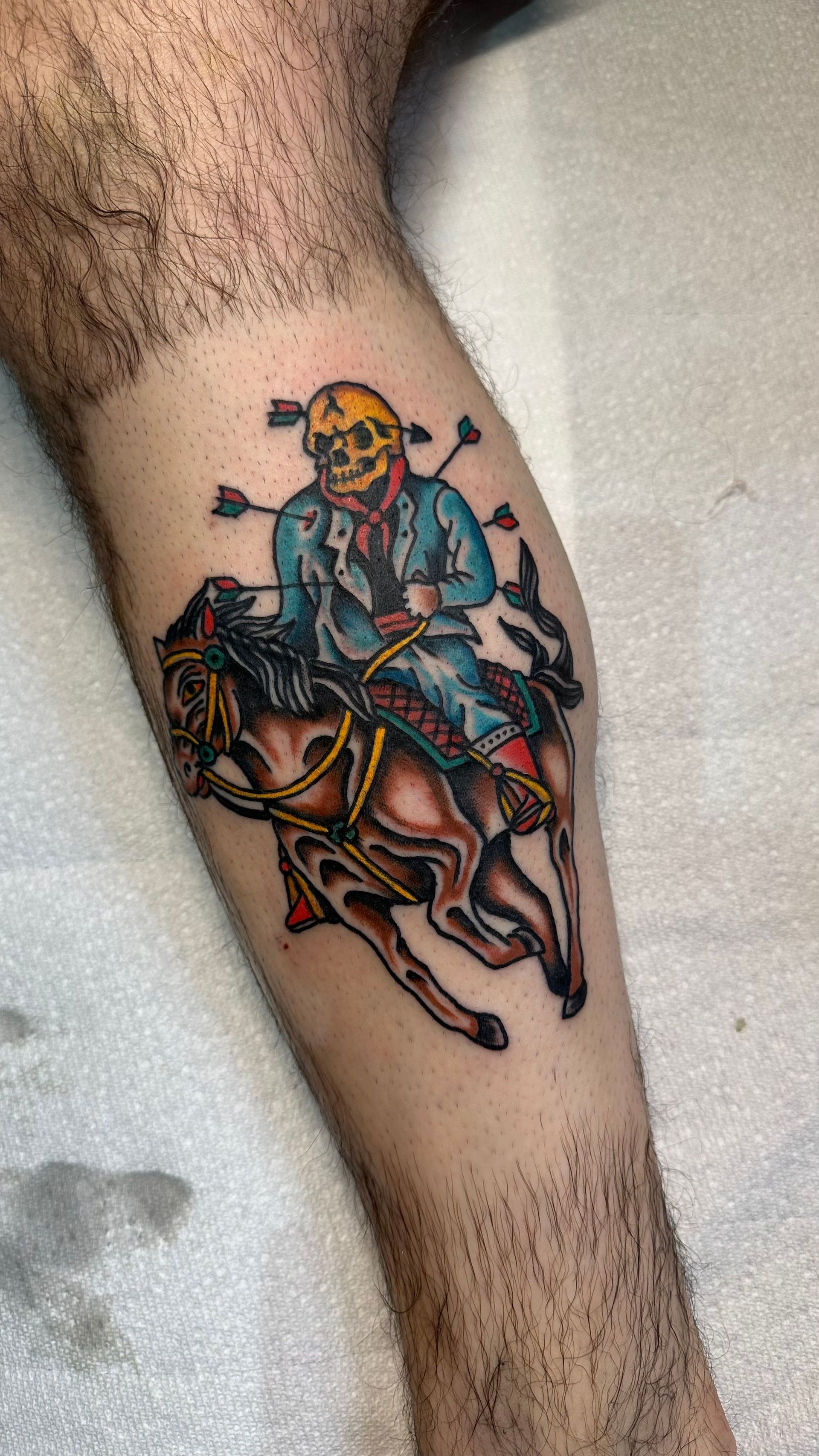 Tattoo of a skeletal rider pierced by arrows on a galloping brown horse; blue jacket, yellow skull.