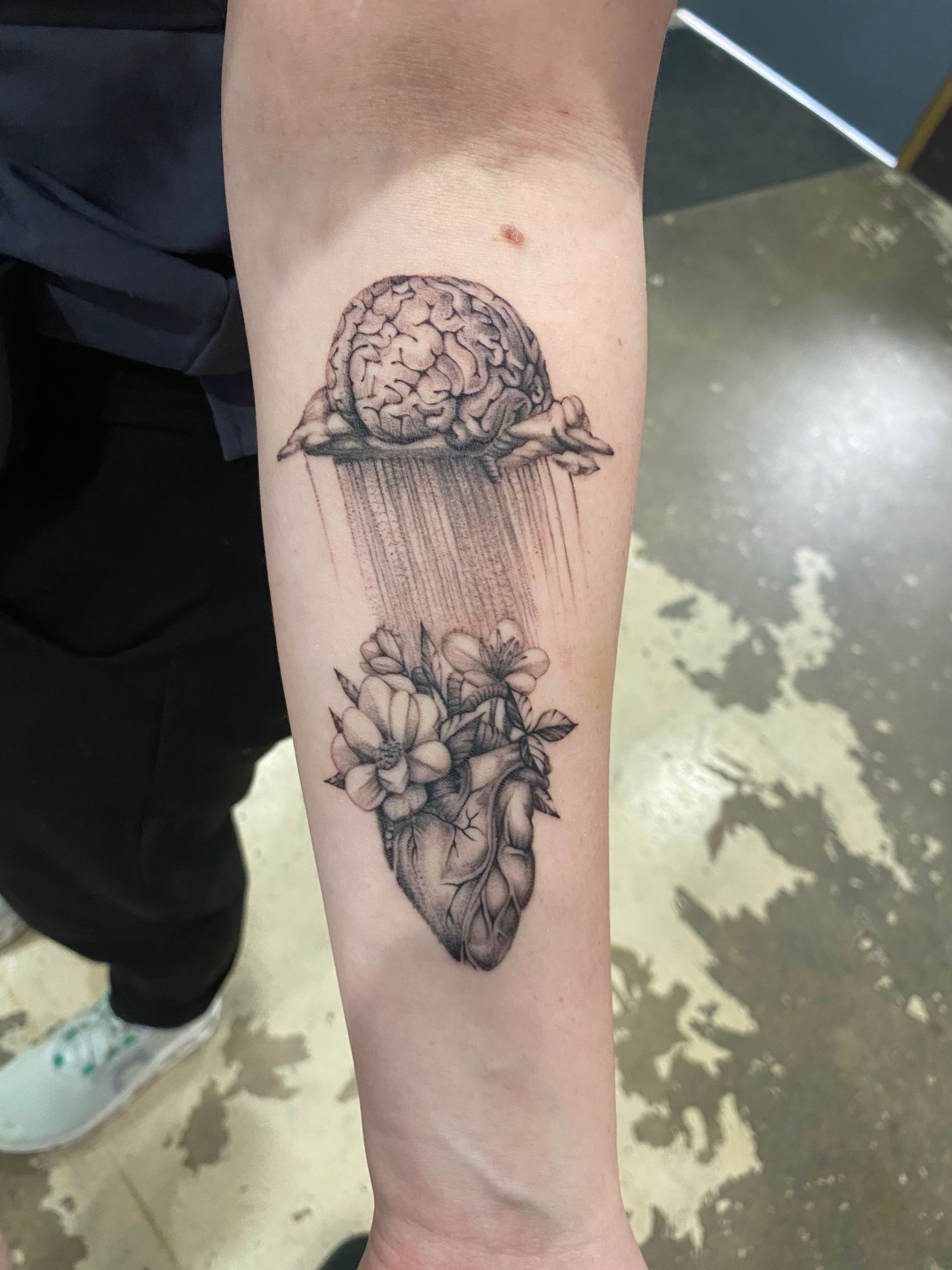 Brain and heart tattoo with floral accents on the forearm, completed at a custom tattoo shop in North Carolina.