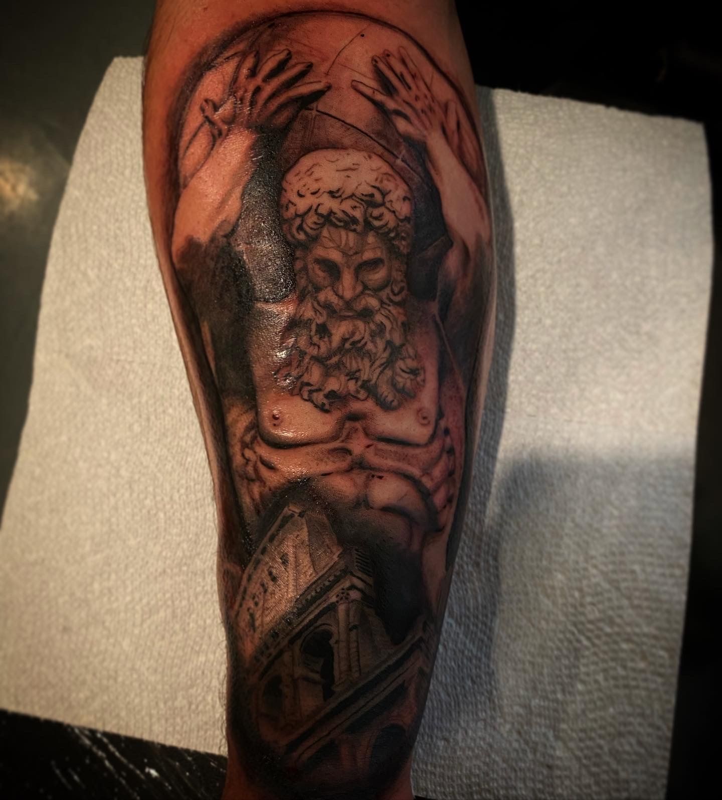 Black and grey Atlas tattoo design on calf with a detailed architectural element, created by a top tattoo artist in Raleigh.