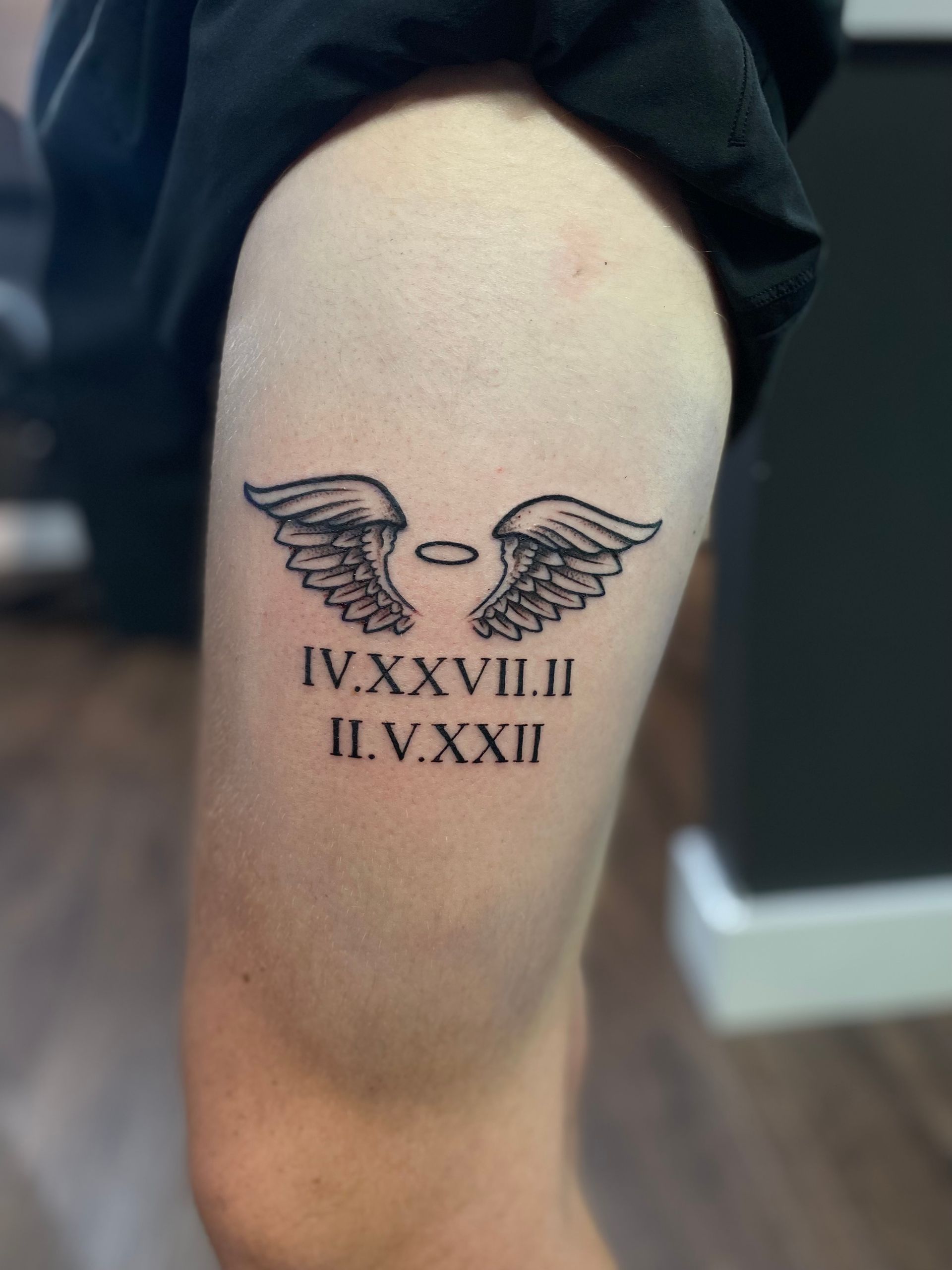 Black and grey angel wings with Roman numerals on thigh, realism tattoo in Raleigh.