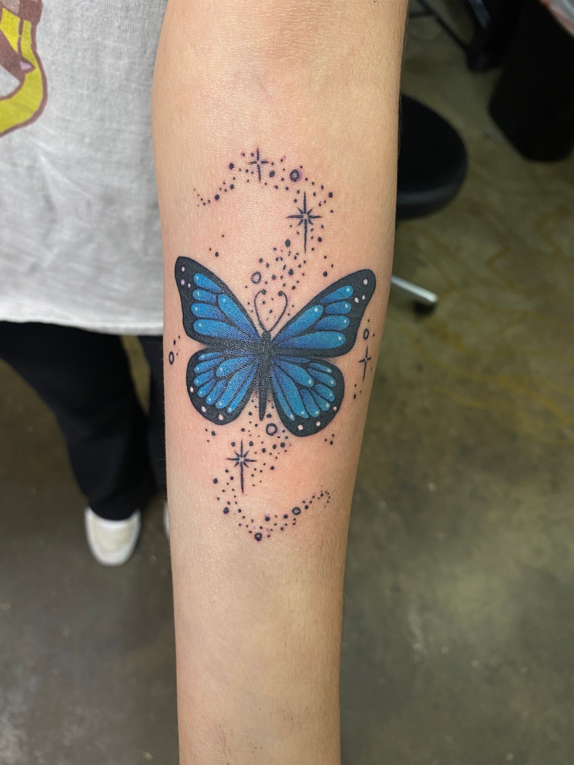 Blue butterfly tattoo surrounded by star details. A beautiful forearm piece from a top tattoo parlor in Raleigh, NC.