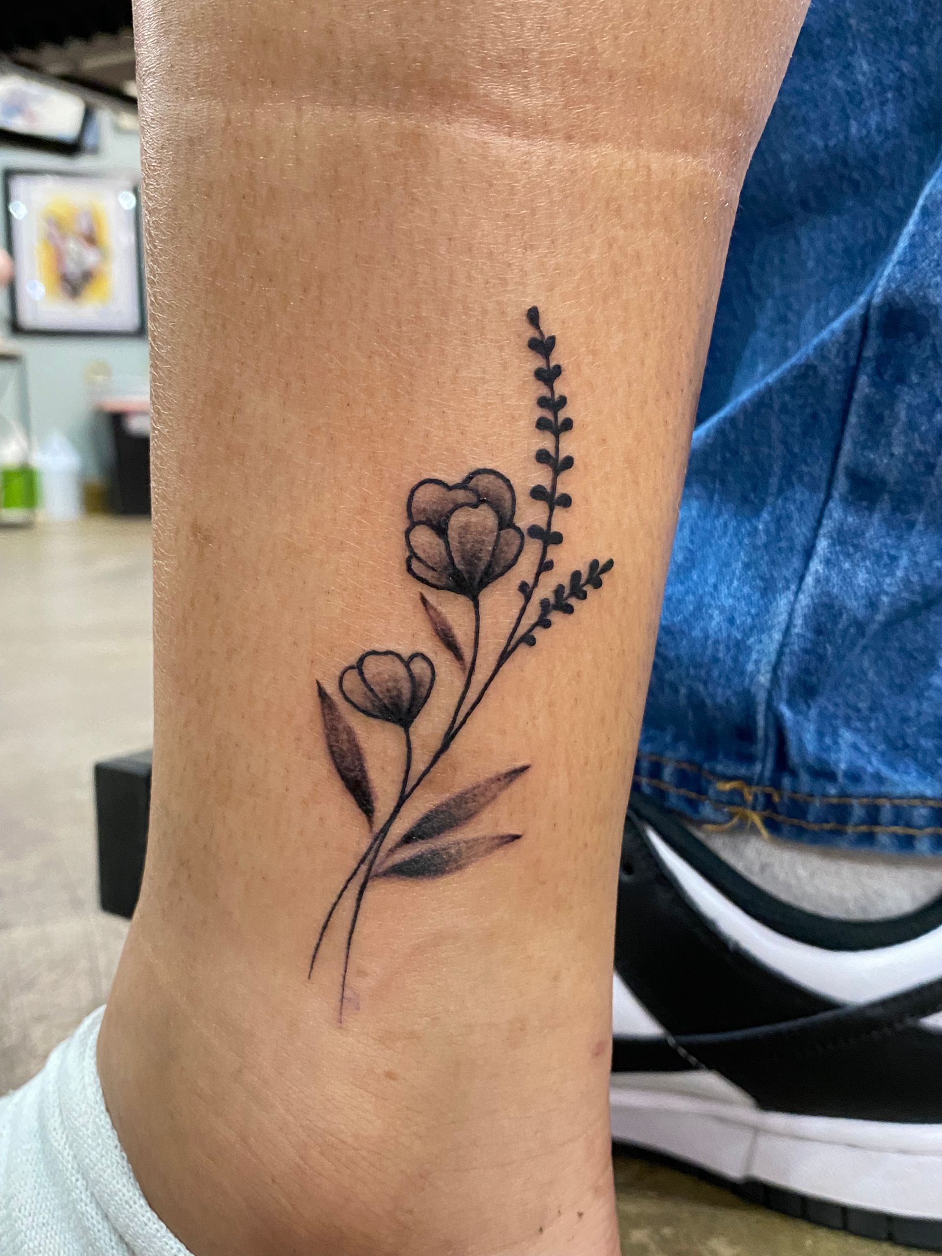 Black and grey flower ankle tattoo, fine line realism design in Raleigh.