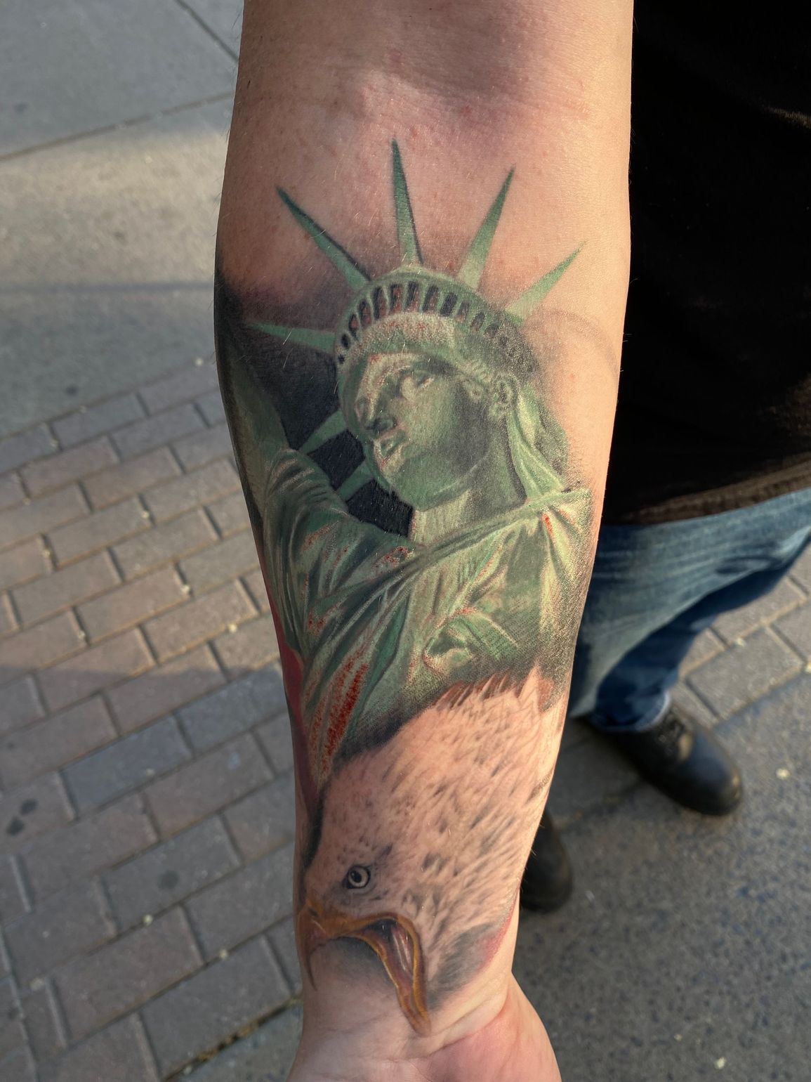 Statue of Liberty forearm tattoo with eagle design, realistic style.