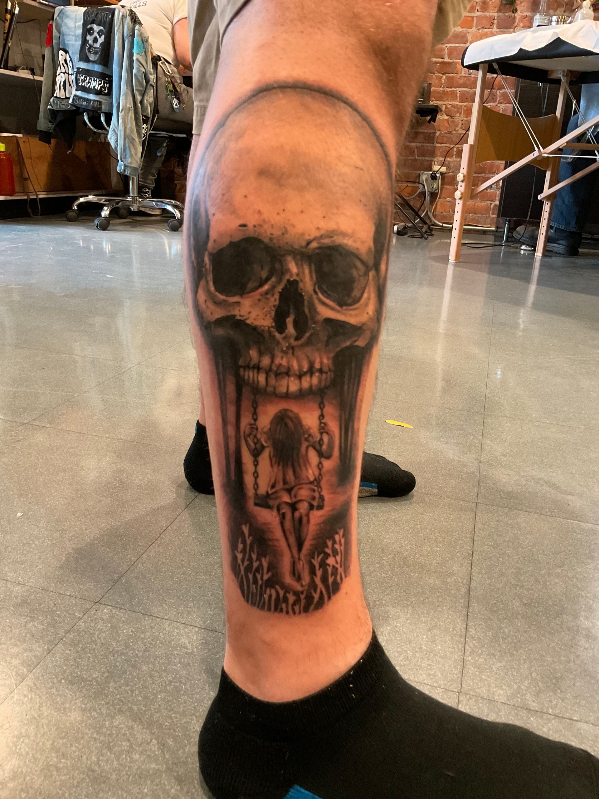 Black and grey realism skull tattoo with a girl on a swing, designed at one of the best tattoo shops. Forearm tattoo for men.