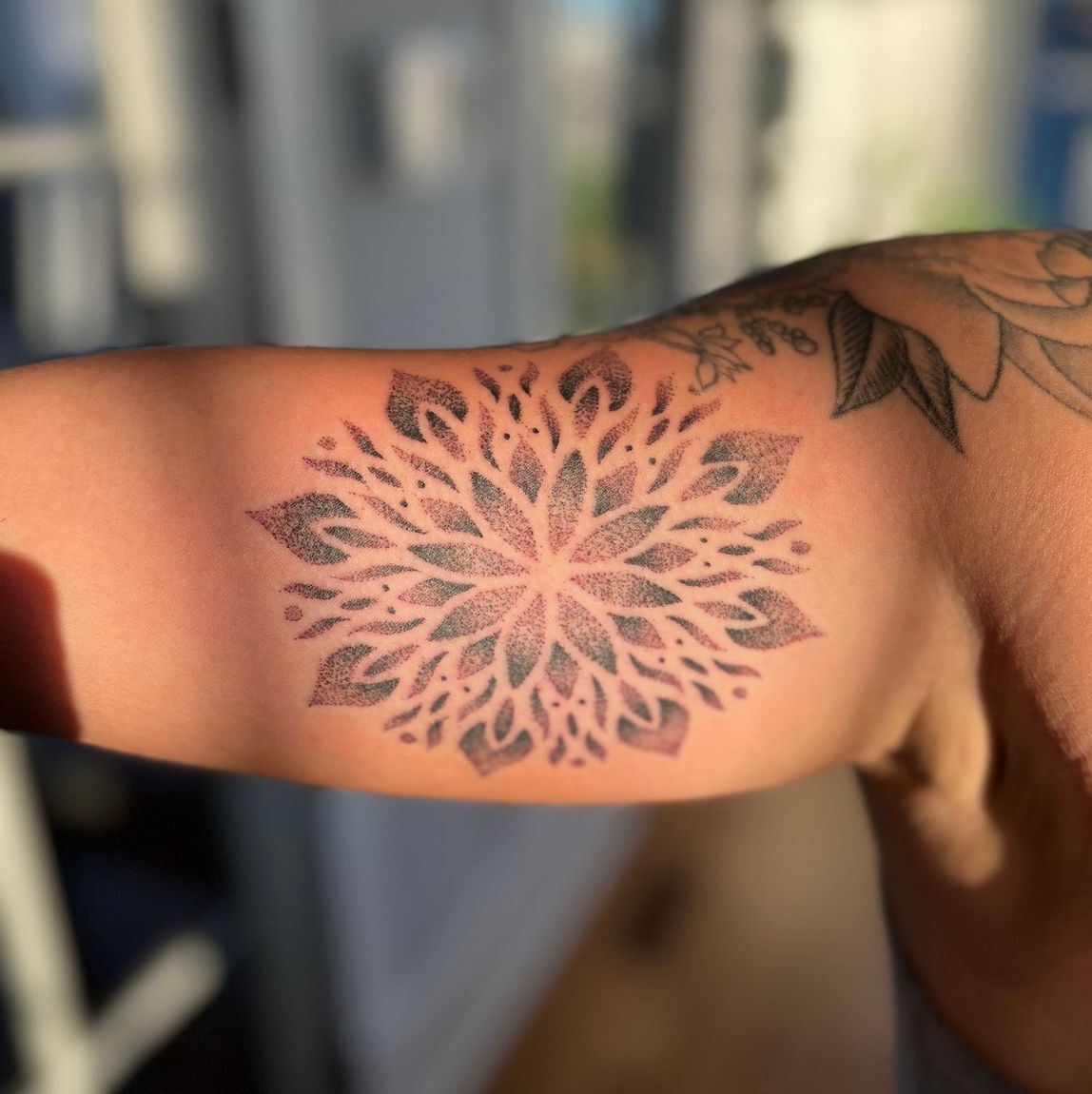 Black and grey mandala tattoo on bicep, showcasing detailed dot work.