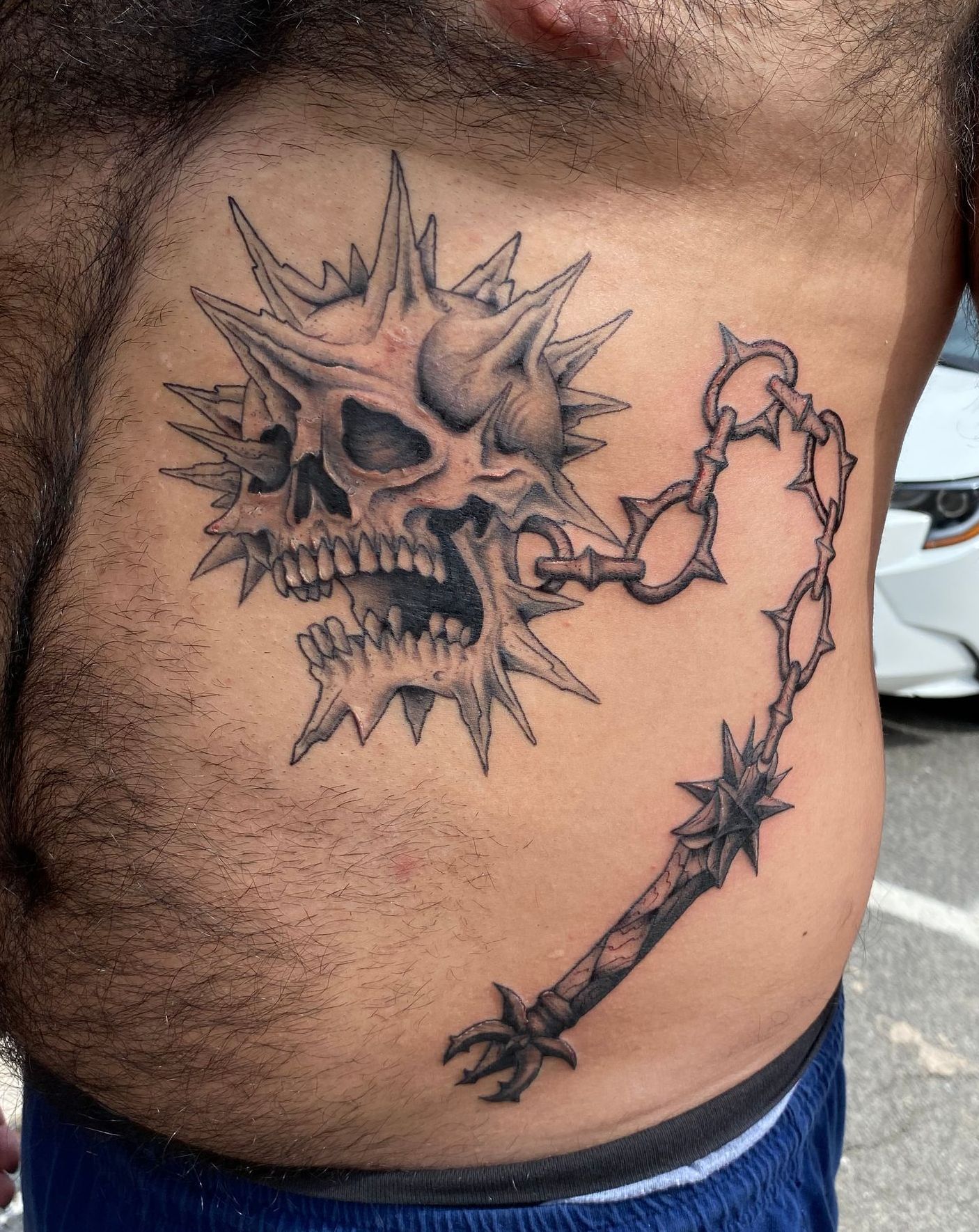 Black and gray tattoo of a spiked skull and mace on ribs, made by a talented tattoo artist in Raleigh NC.