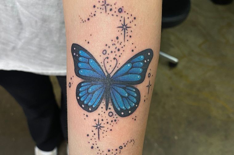 Colorful blue butterfly tattoo with star details on forearm.