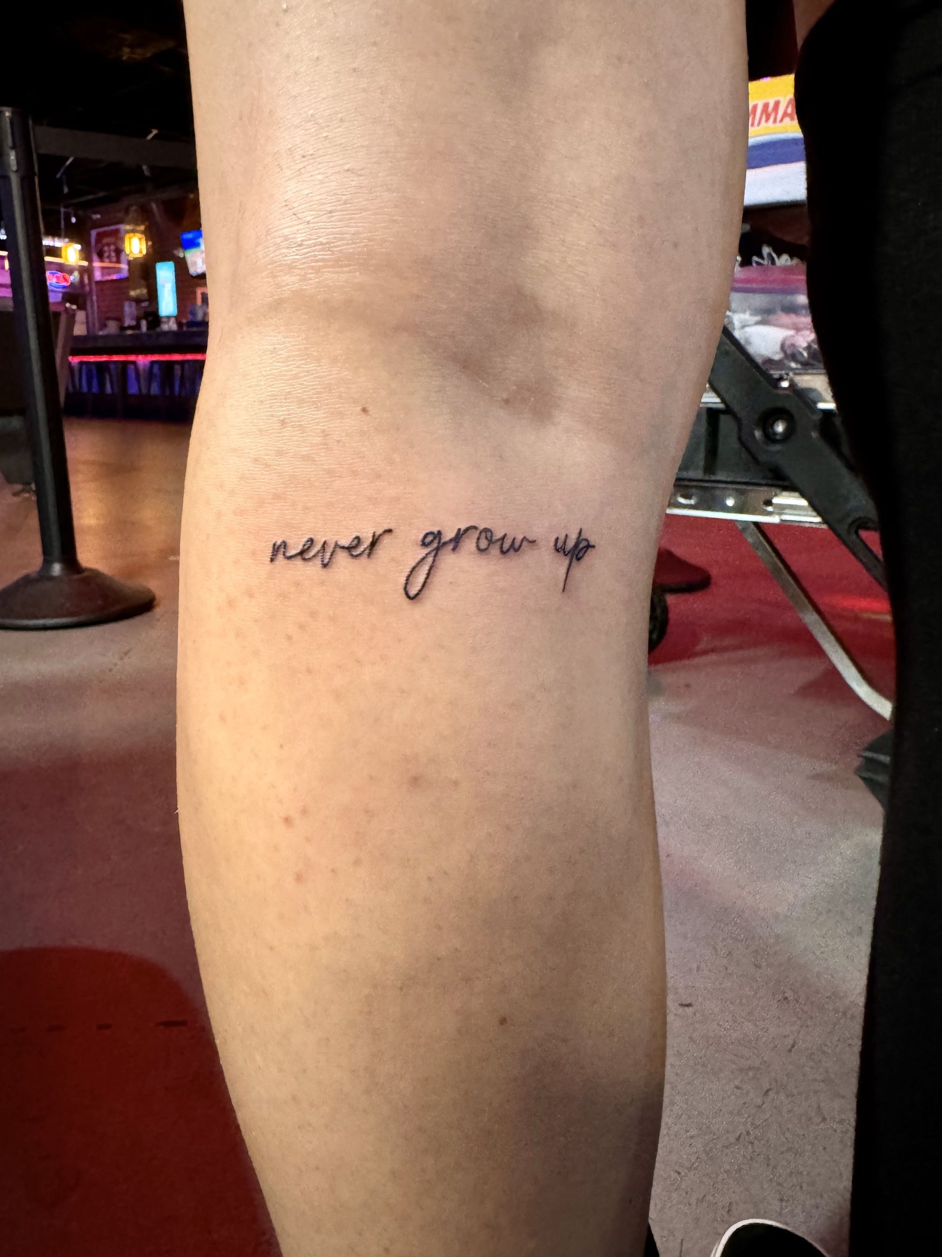 Freshly inked 'never grow up' text tattoo at TEETS X Aether event, done in a clean, simple script style